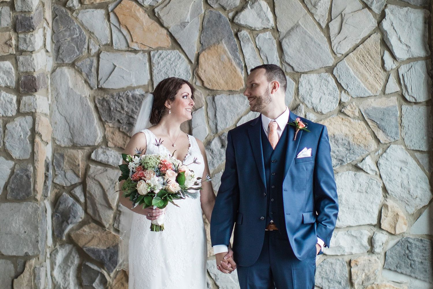 Couple poses against stone wall backdrop at wedding venue.