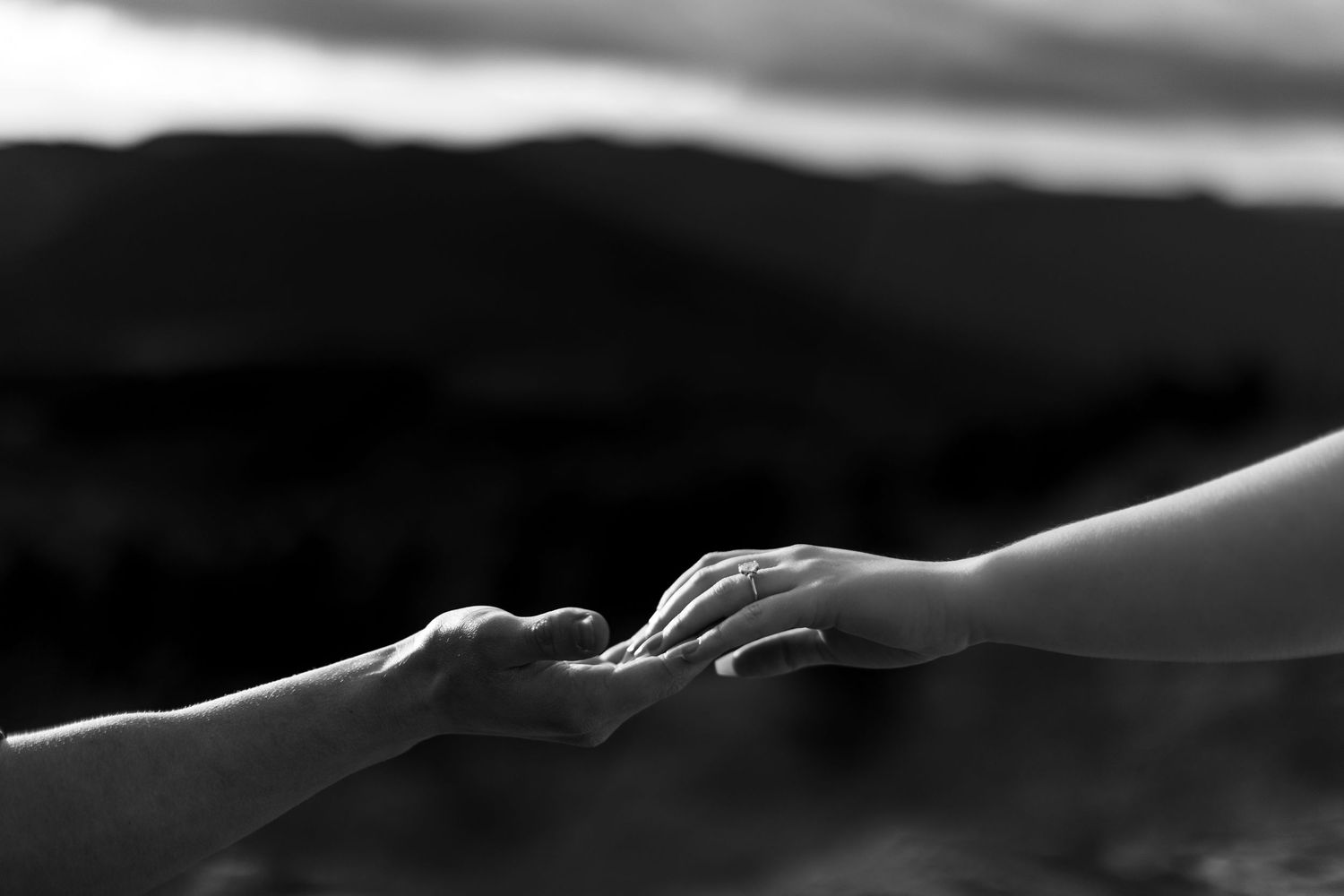 Two hands reaching out to hold each other in a tender gesture against a dark blurred background.