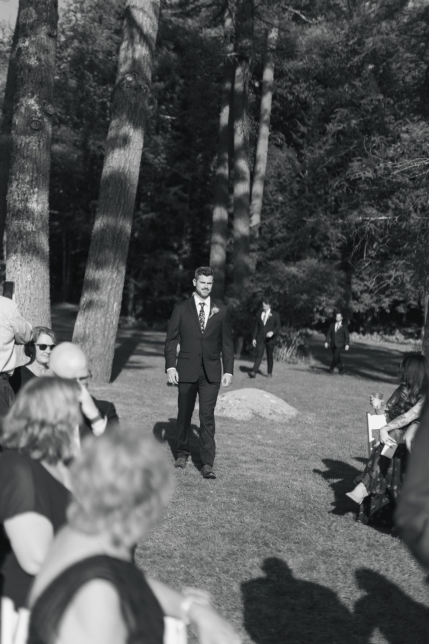 A black and white photo of a wedding ceremony processional among tall pine trees.