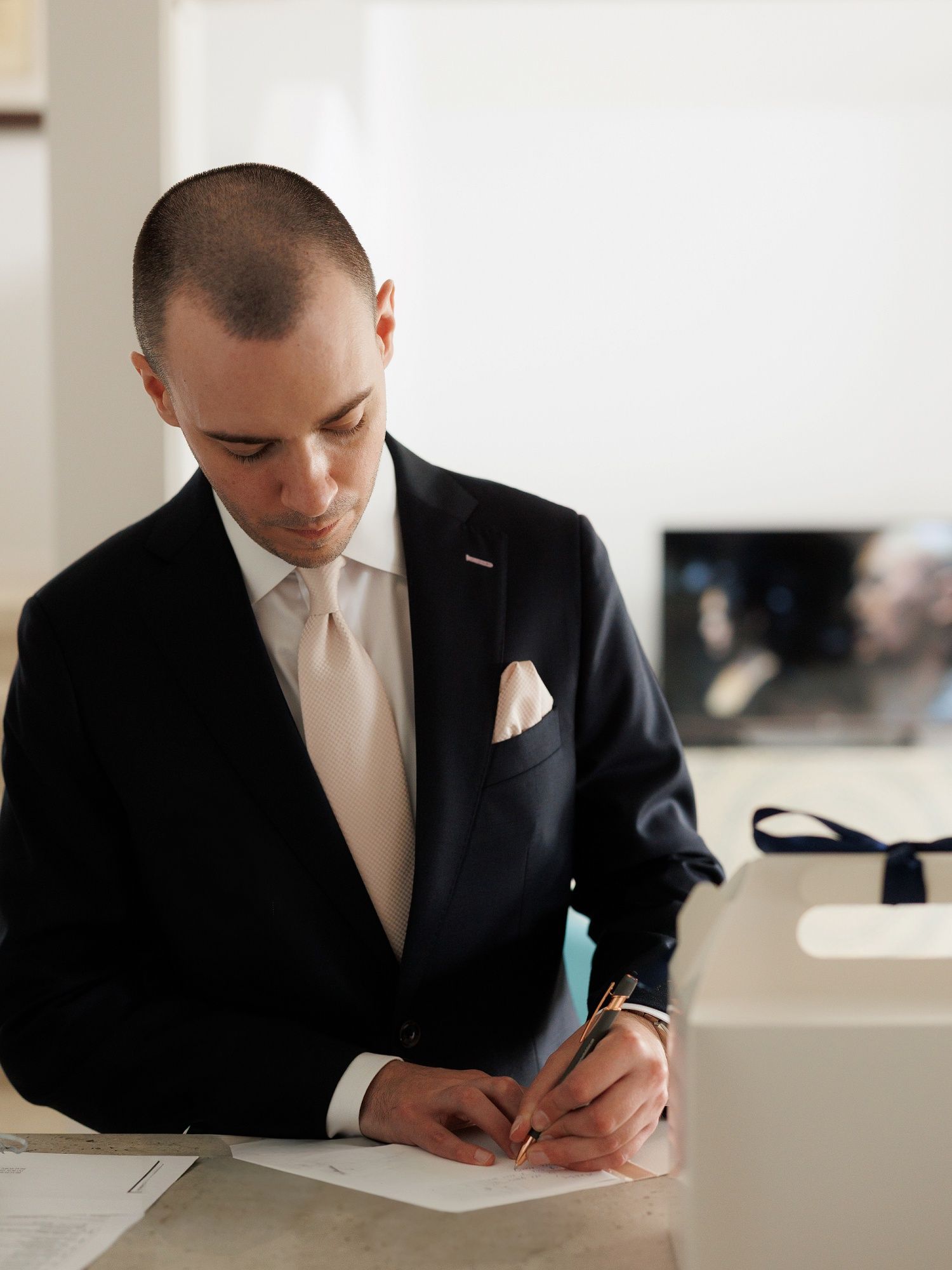 Professional in dark suit signs important documents at bright white desk in modern office setting.