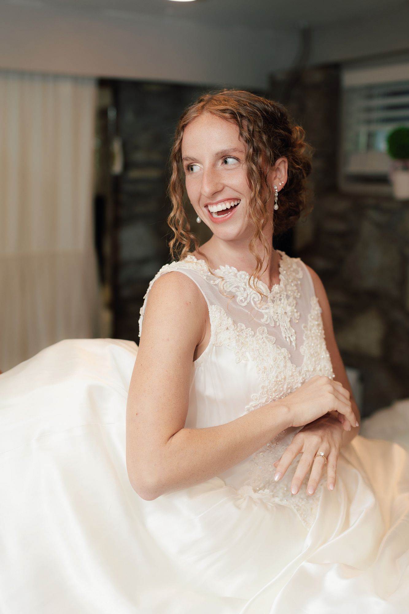 Happy bride in lace wedding gown smiling joyfully while getting ready for her wedding day.