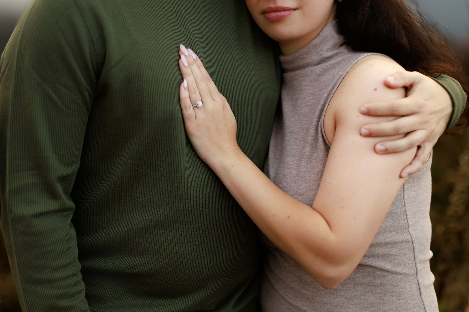 An intimate embrace showing a green sweater and beige turtleneck against a light background.