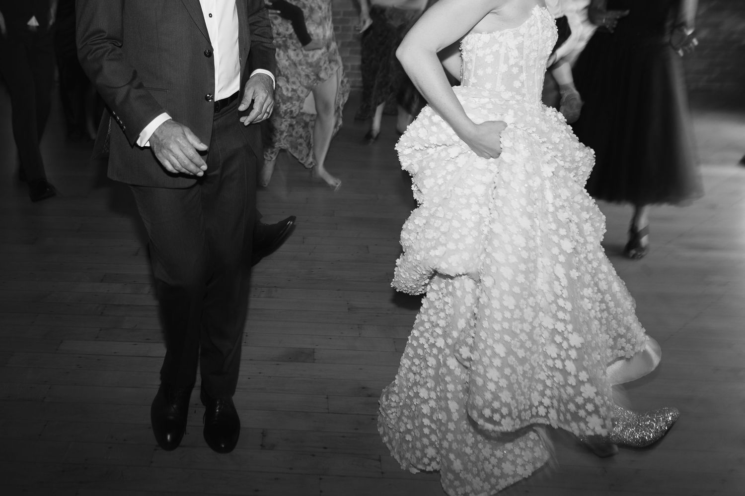 Black and white photo of a bride in a ruffled gown and groom in tuxedo dancing at a wedding reception.