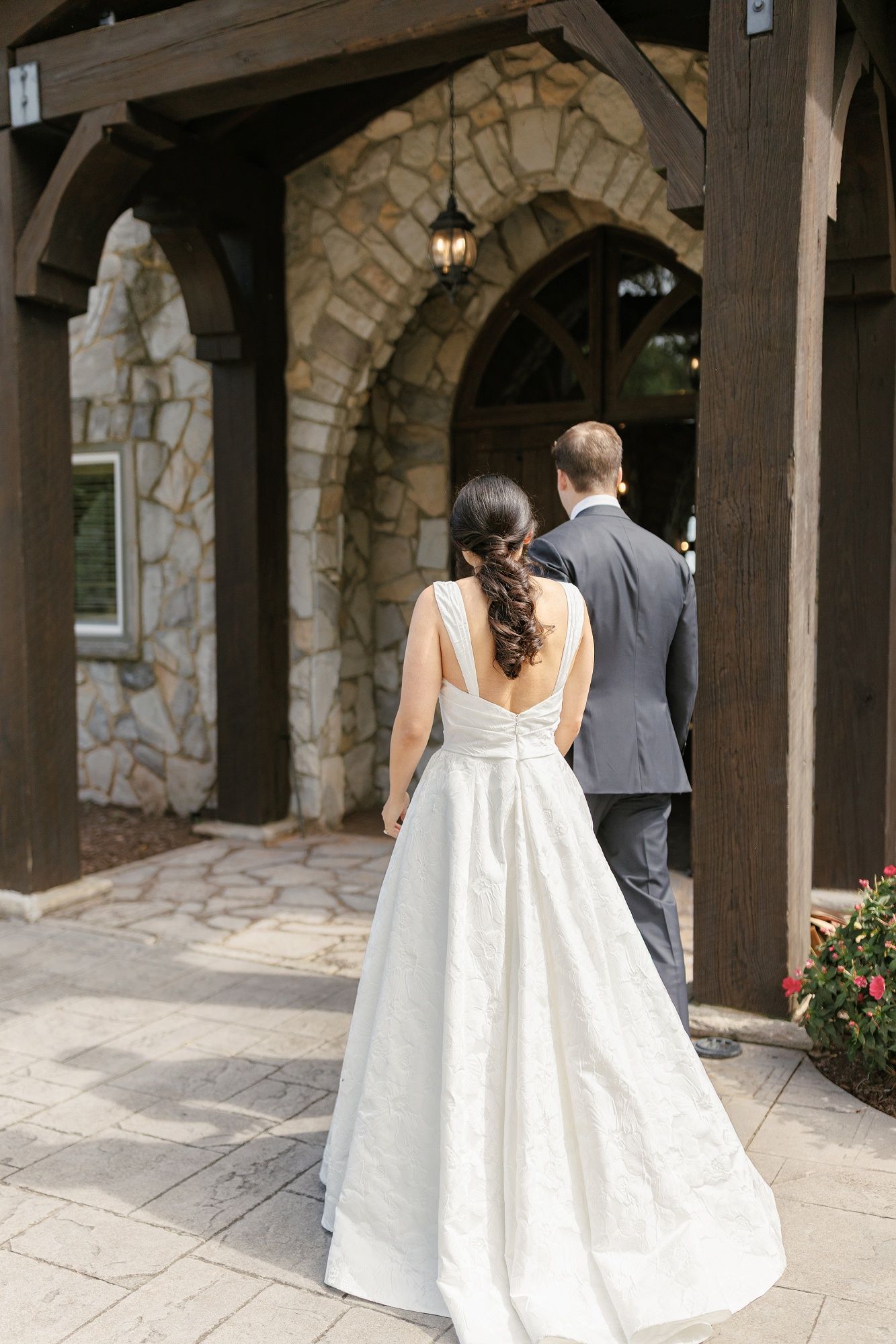 A couple walks under a covered stone archway during their wedding day.