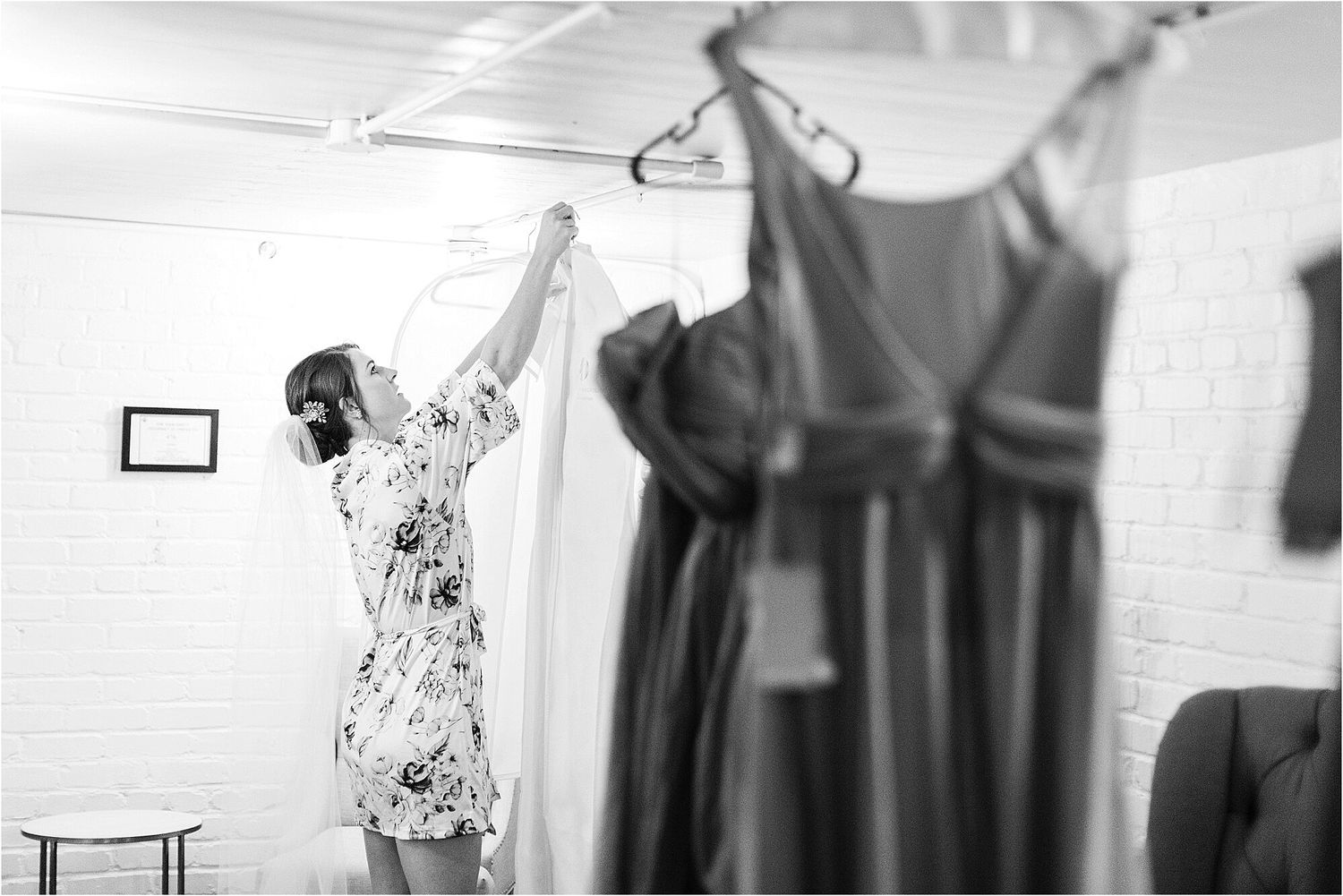Wedding preparation scene in bright white room with dresses hanging.