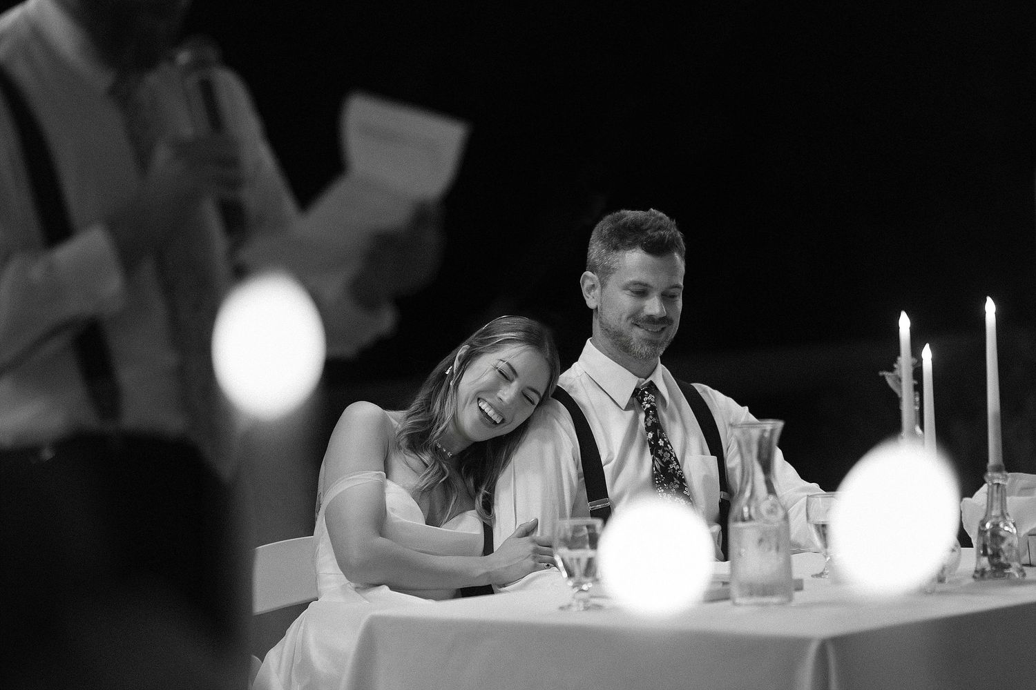 Candlelit wedding reception table with couple resting during evening celebration.