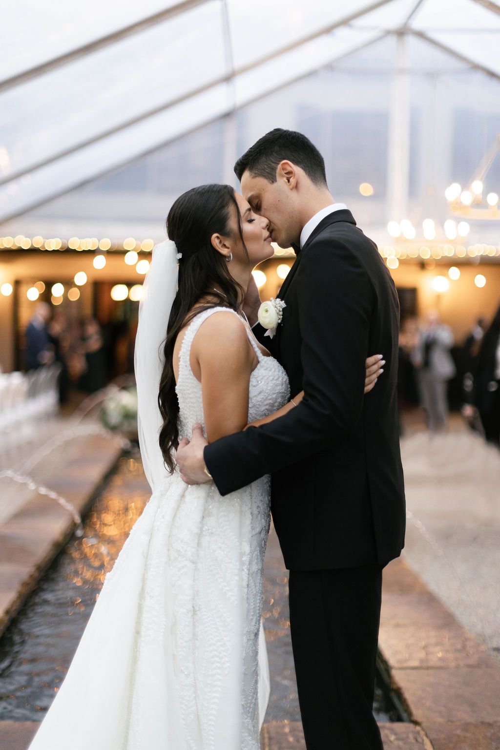 A tender moment between newlyweds under a tent with twinkling lights in the background.