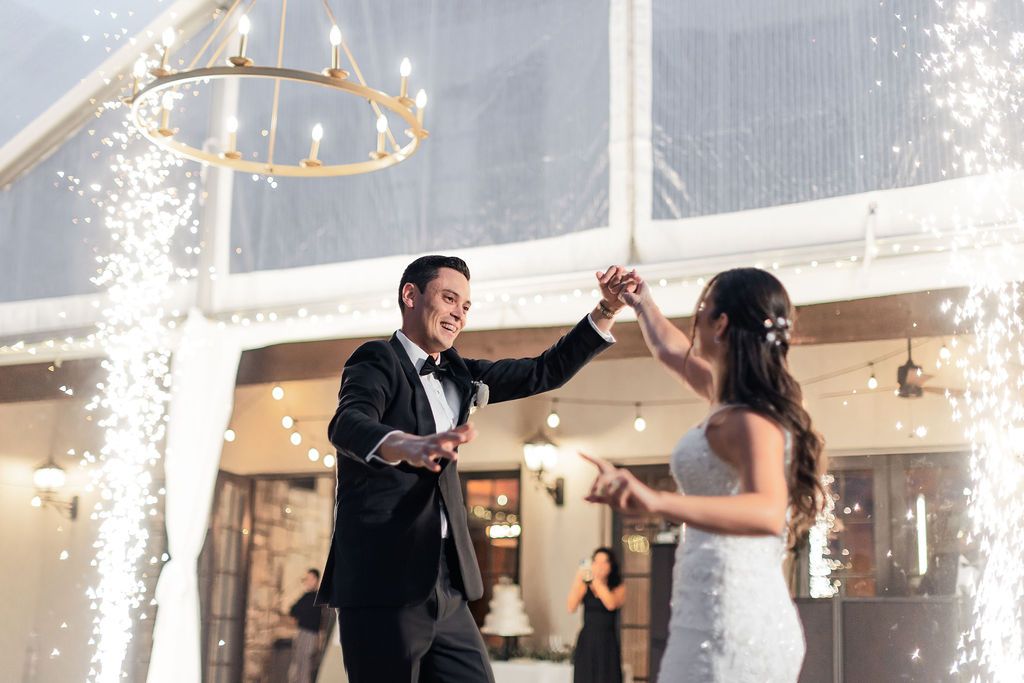 Newlyweds dancing with sparklers in background at outdoor tent reception.