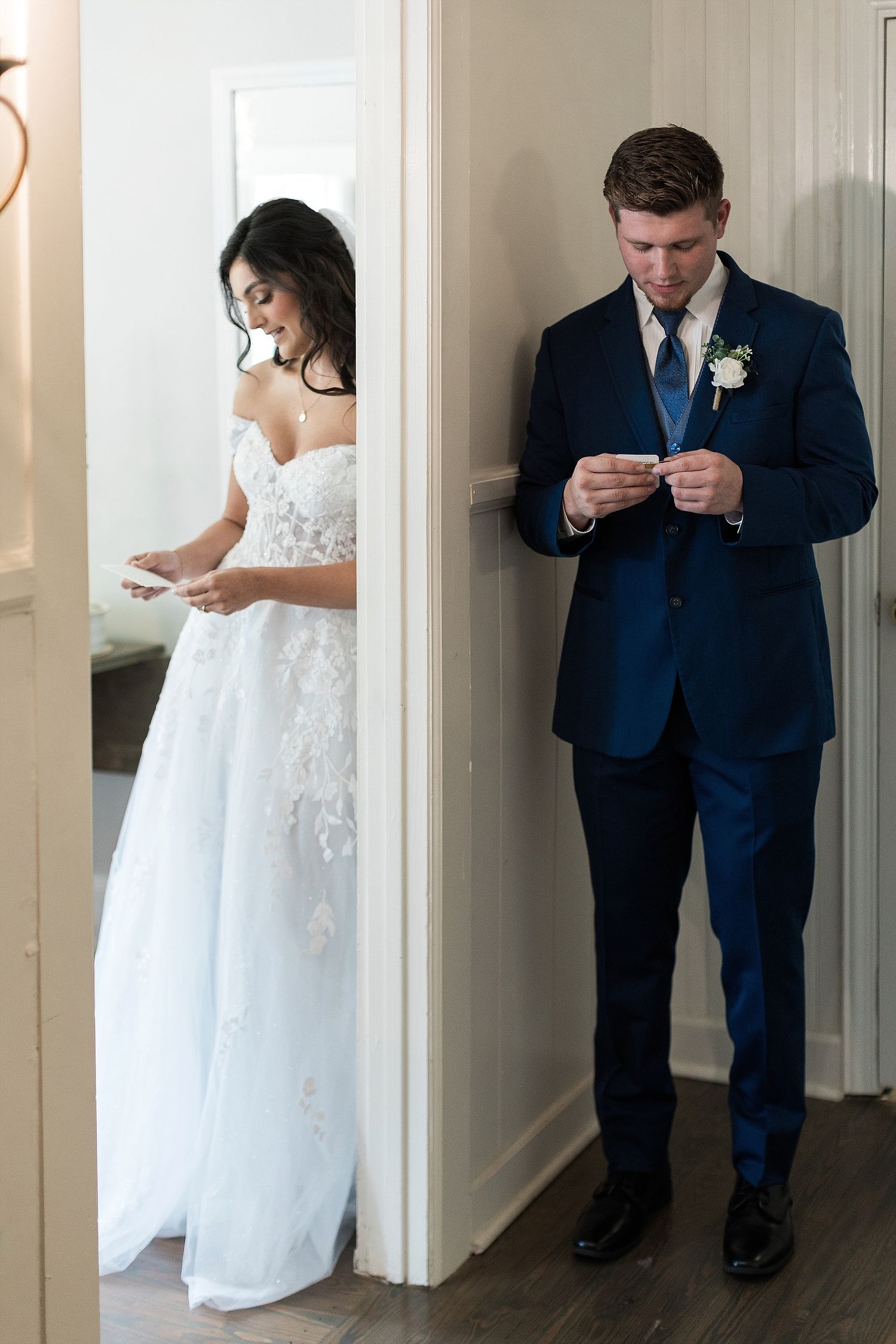 Couple reads letters while separated by wall, bride in white dress and groom in navy suit.
