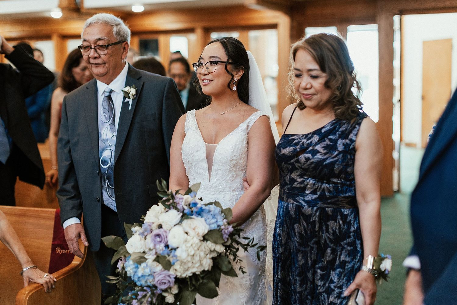 Family members stand with bride holding purple and white bouquet in church setting.