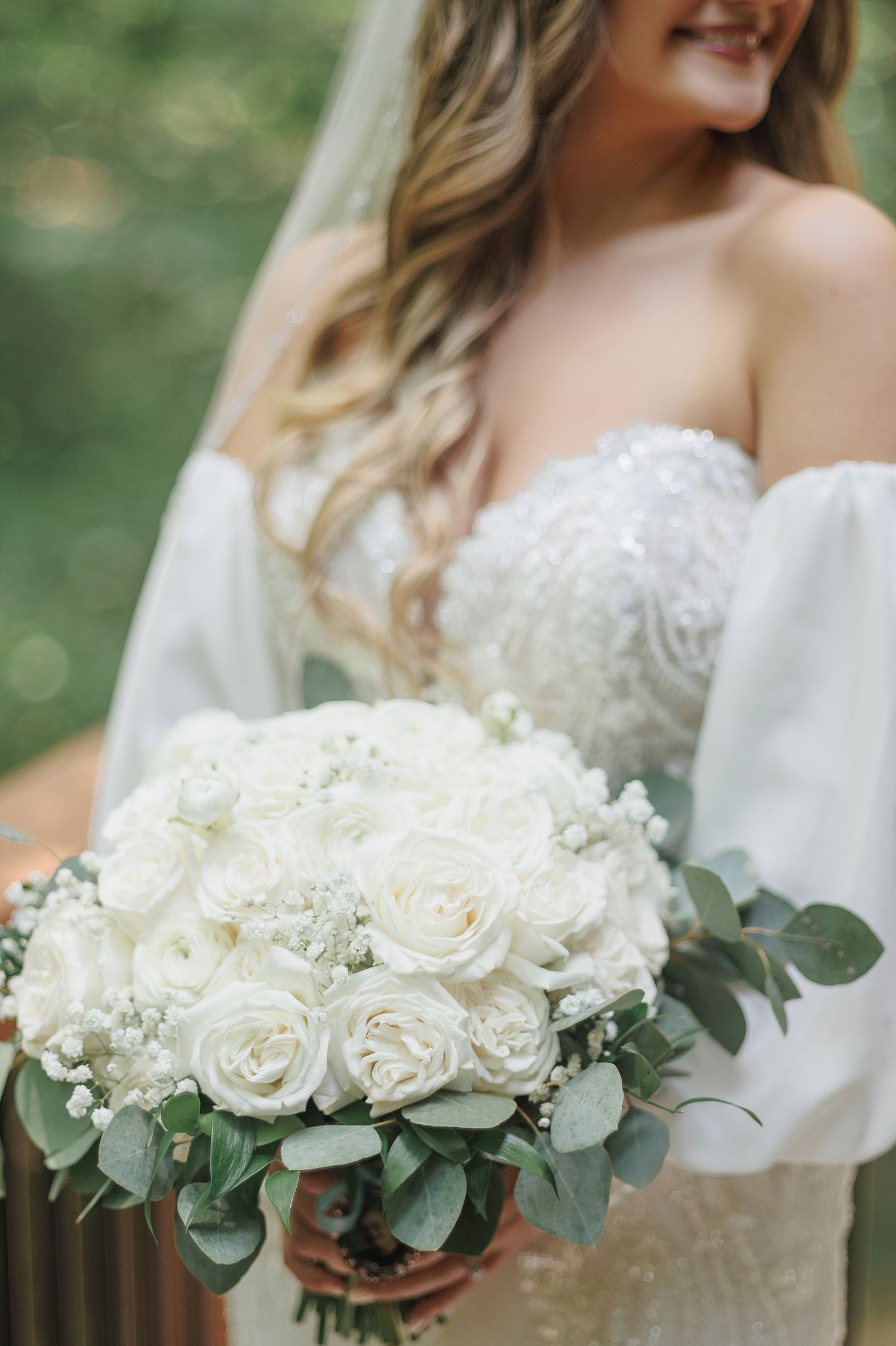 Close-up of a white rose and eucalyptus bridal bouquet with lace wedding dress detail.
