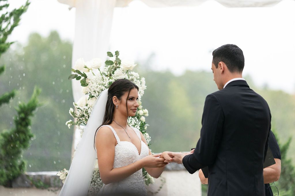 Wedding ceremony exchange of rings under white floral arch.