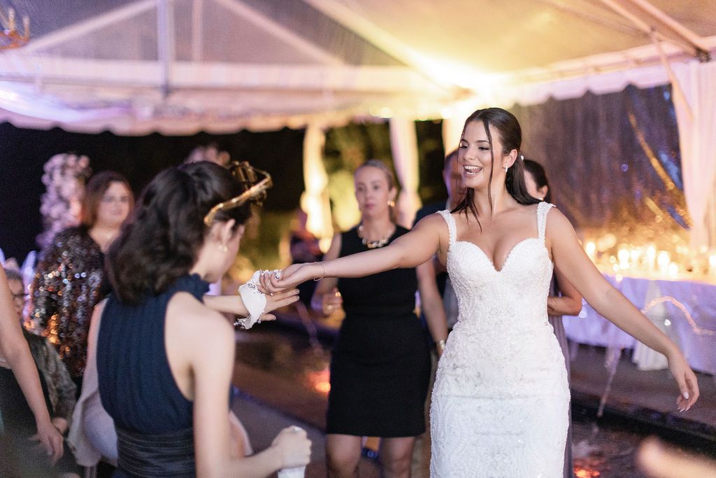 Wedding celebration with guests dancing under a white tent with ambient lighting.