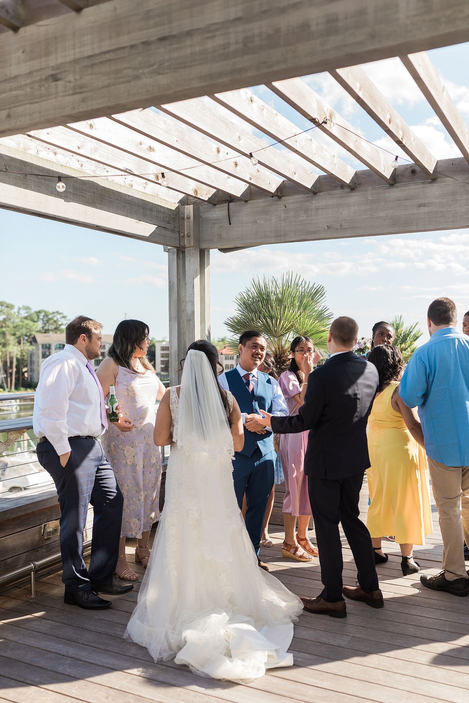 Wedding reception gathering on a covered deck with palm trees visible in background.