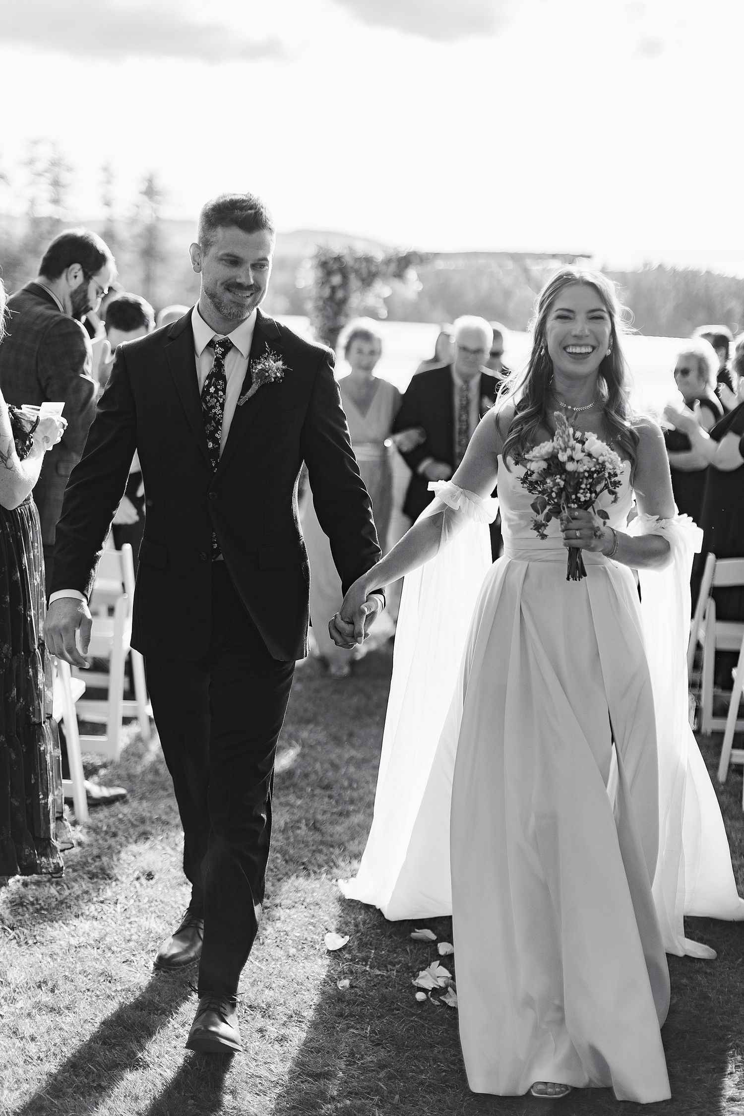 Black and white photo of newlyweds joyfully walking back down the aisle after outdoor wedding ceremony.