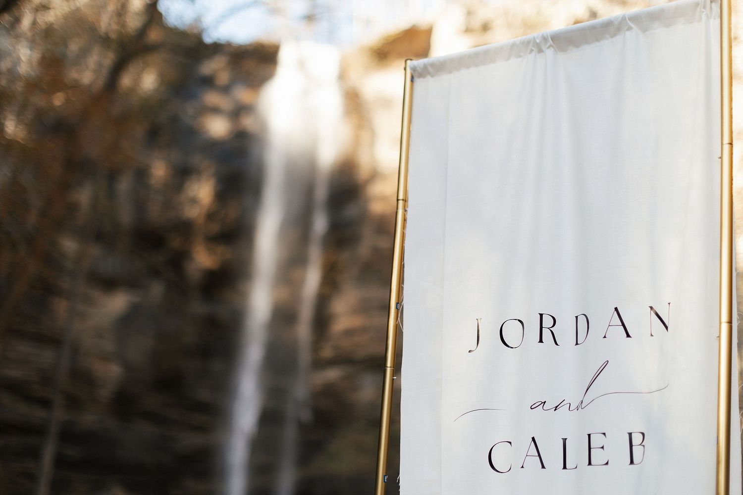 An elegant wedding sign reading 'Jordan and Caleb' displayed at an outdoor venue with natural lighting and rock formations.