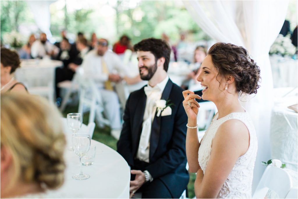 Wedding guests enjoying speeches and toasts during an outdoor tented reception.