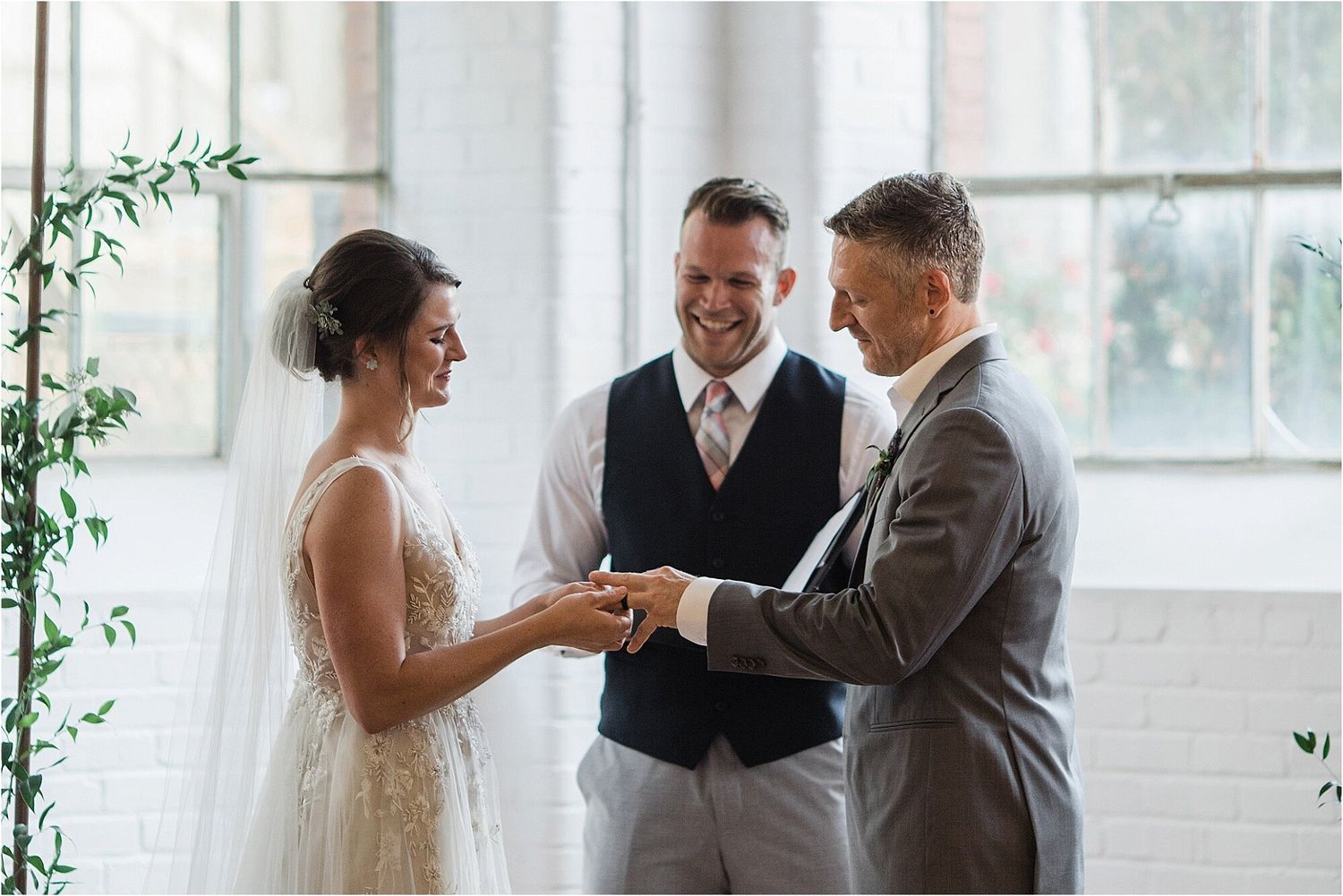 A wedding exchange takes place in front of large windows in a bright, modern venue.