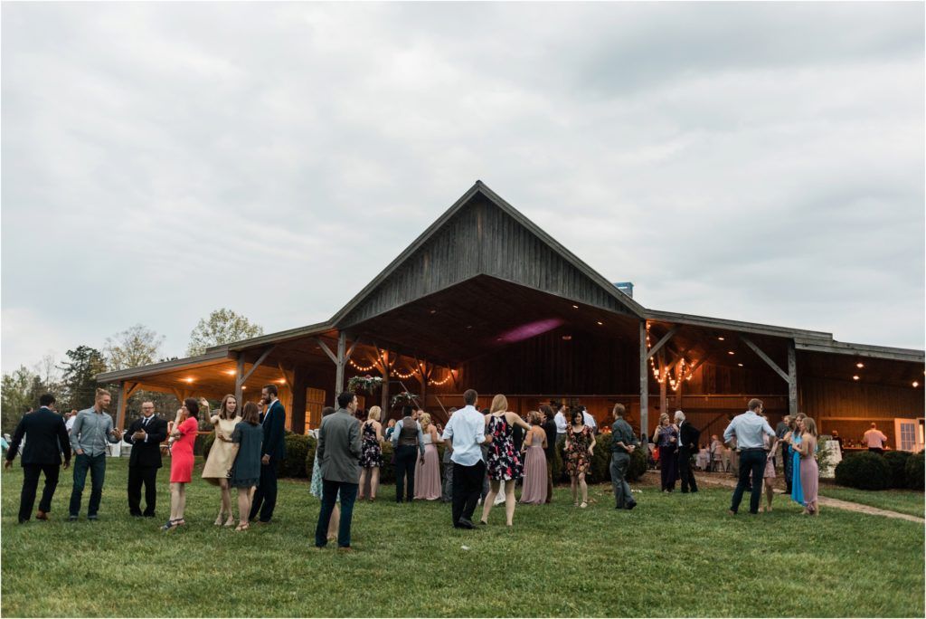 Wedding guests gathered outside a rustic barn venue under cloudy skies.