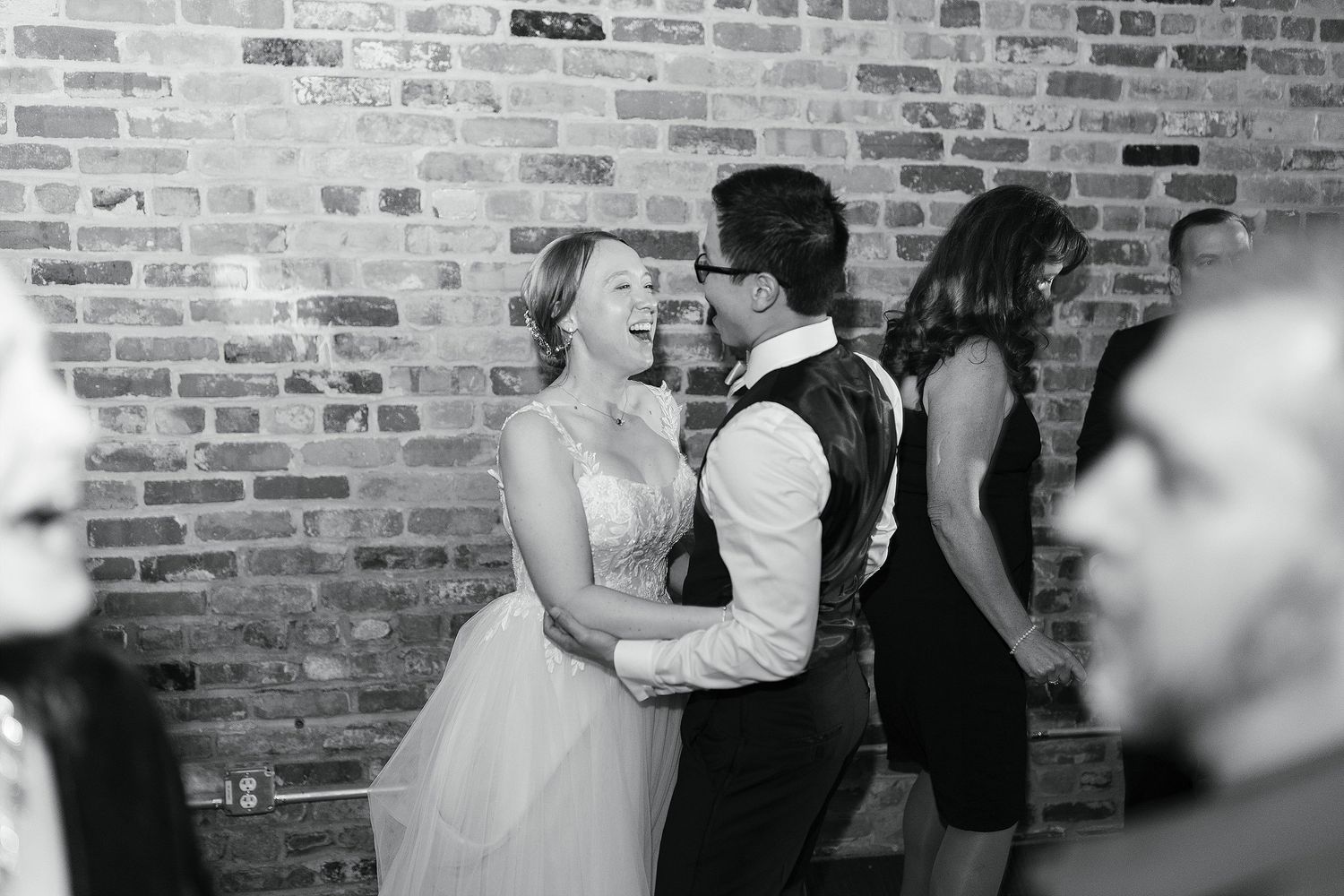 A romantic couple dancing together at a wedding reception against a rustic brick wall background.