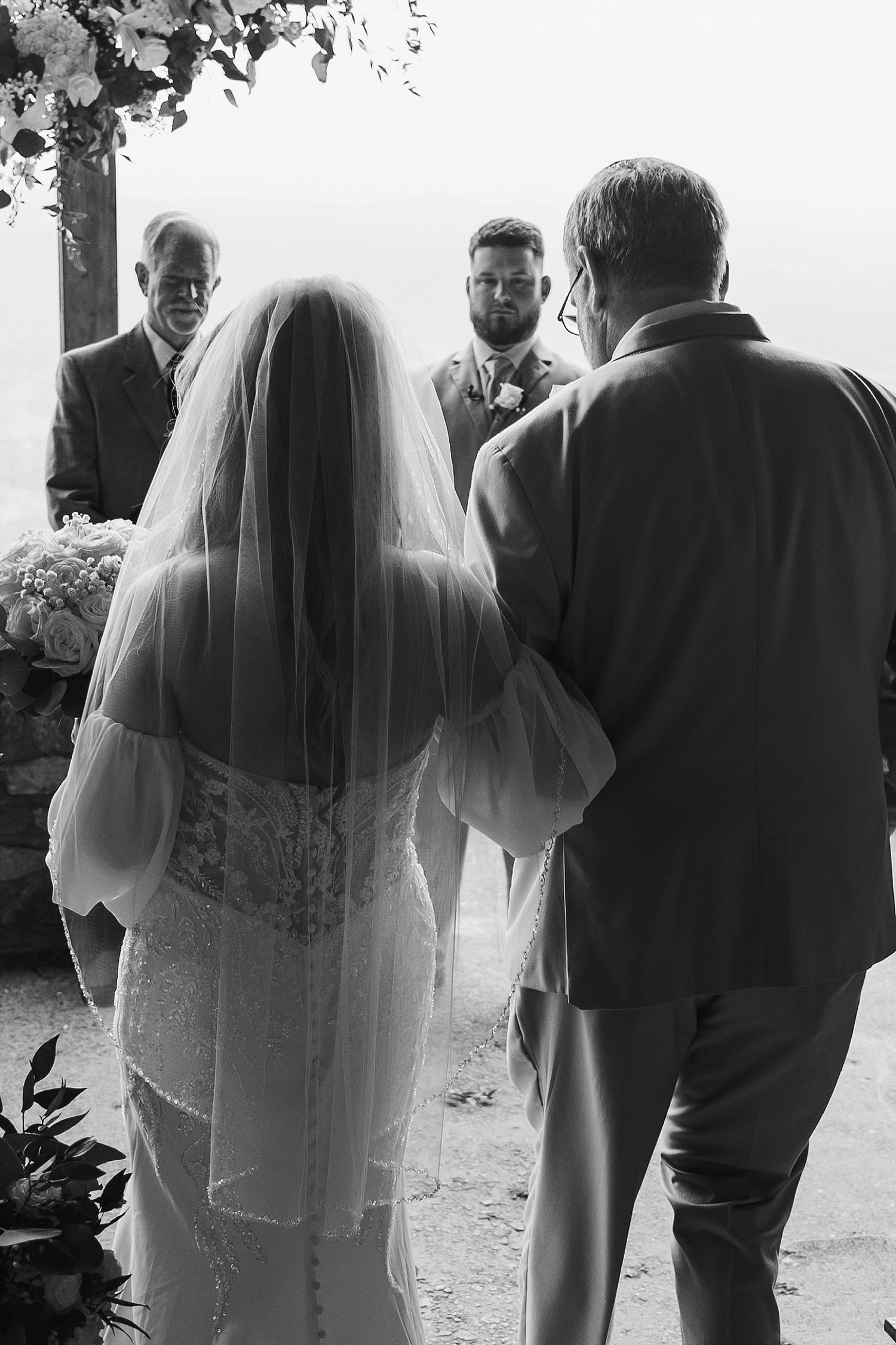 A black and white capture of an intimate wedding ceremony moment under floral decor.