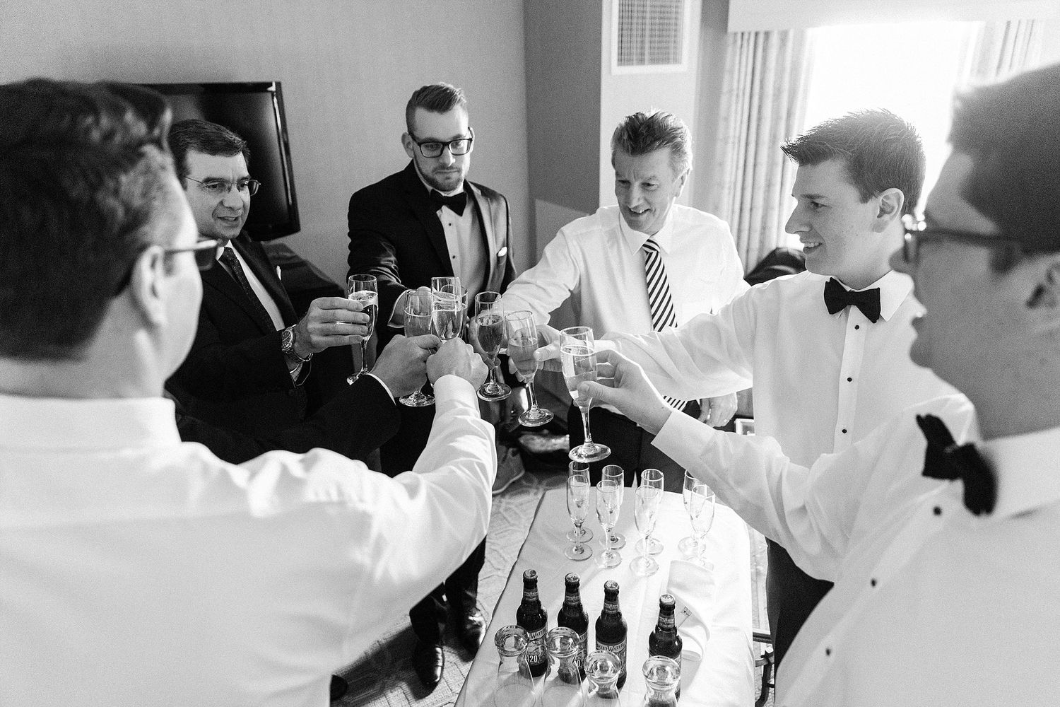 Groomsmen in formal attire gather around for drinks during wedding preparations.