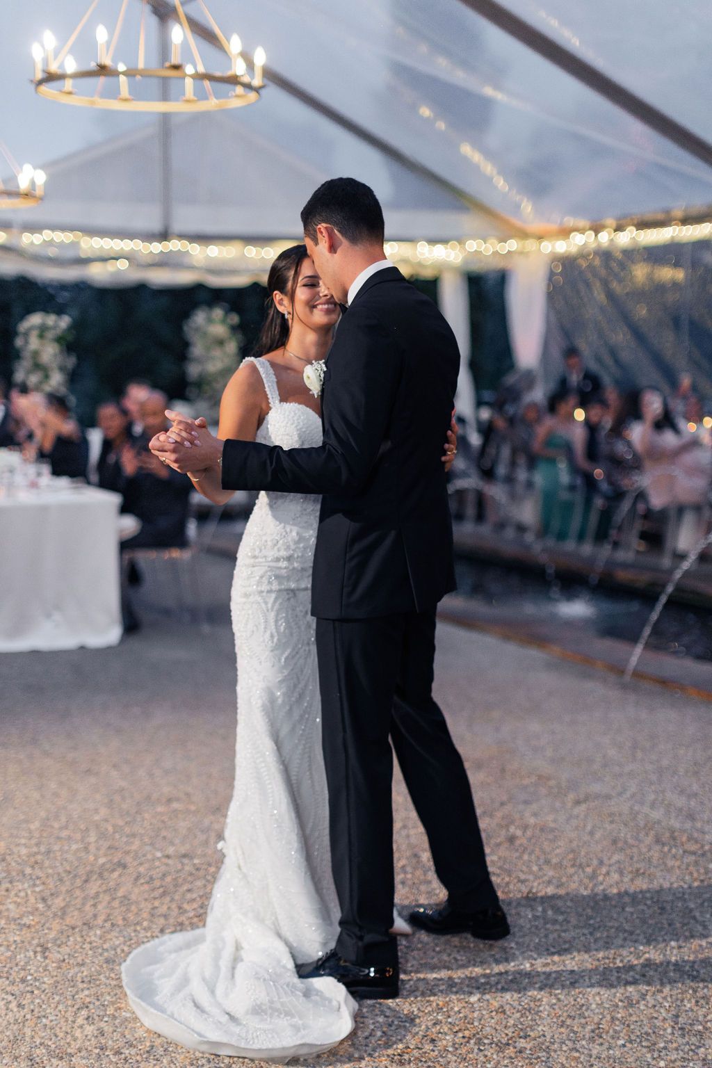 Intimate dance moment captured under elegant lighting in wedding reception tent.