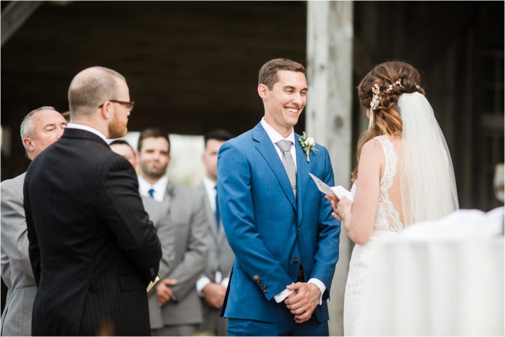 A wedding ceremony takes place under a rustic wooden pavilion with guests watching the exchange of vows.