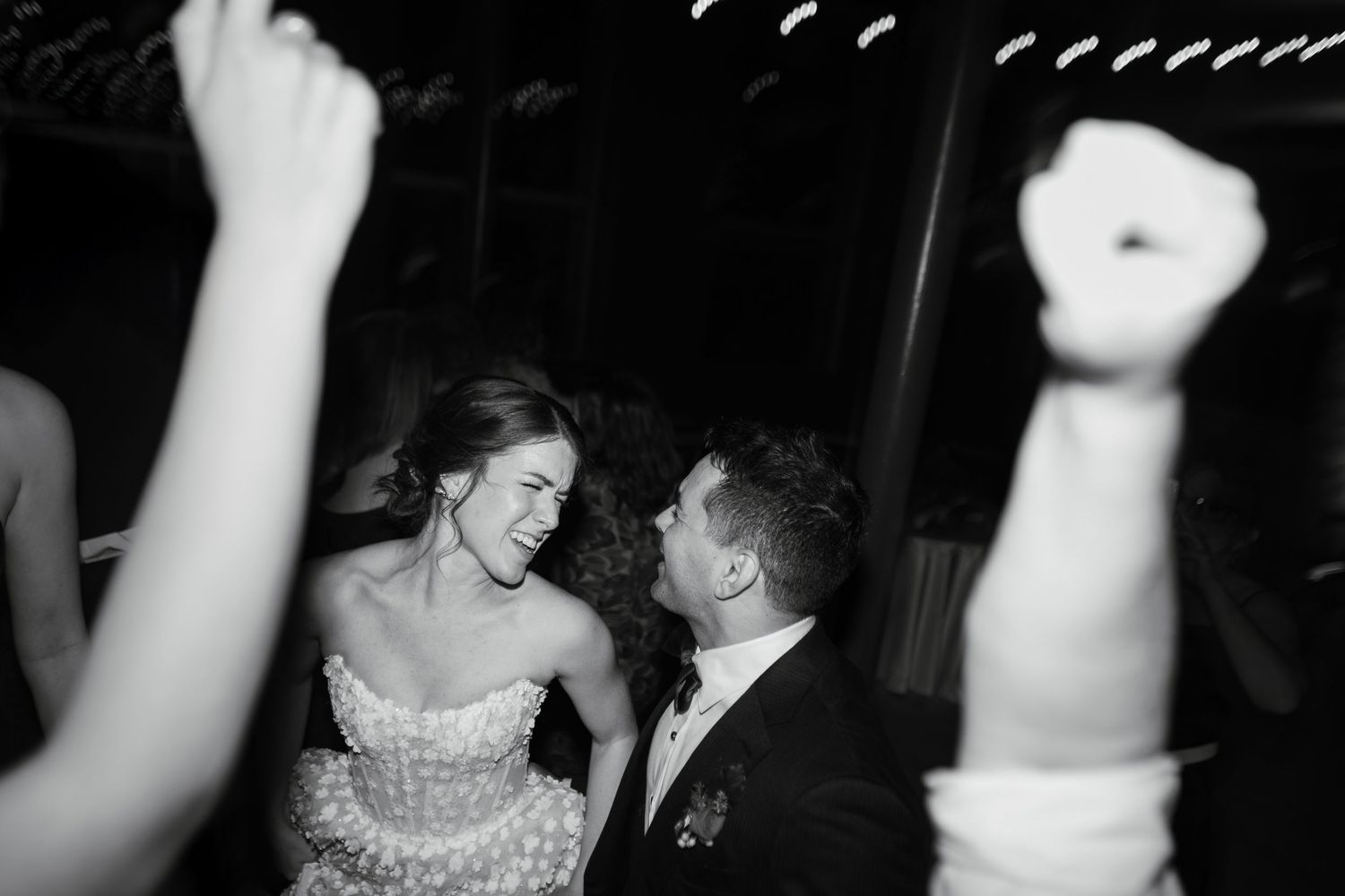 Black and white photo of a bride and groom dancing joyfully at their wedding reception.