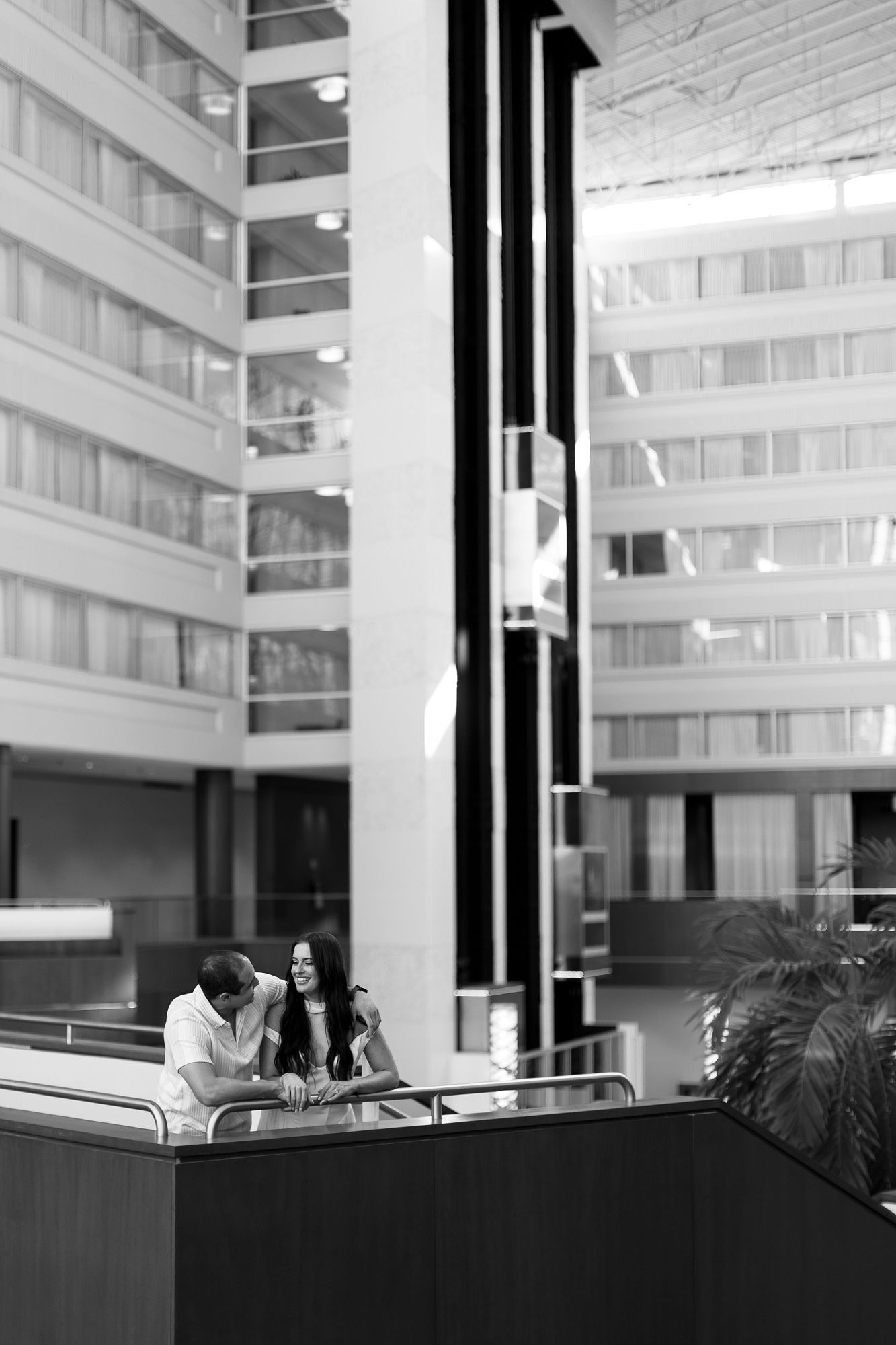 A black and white photo of a couple sitting and talking in a modern atrium with tall white walls and columns.