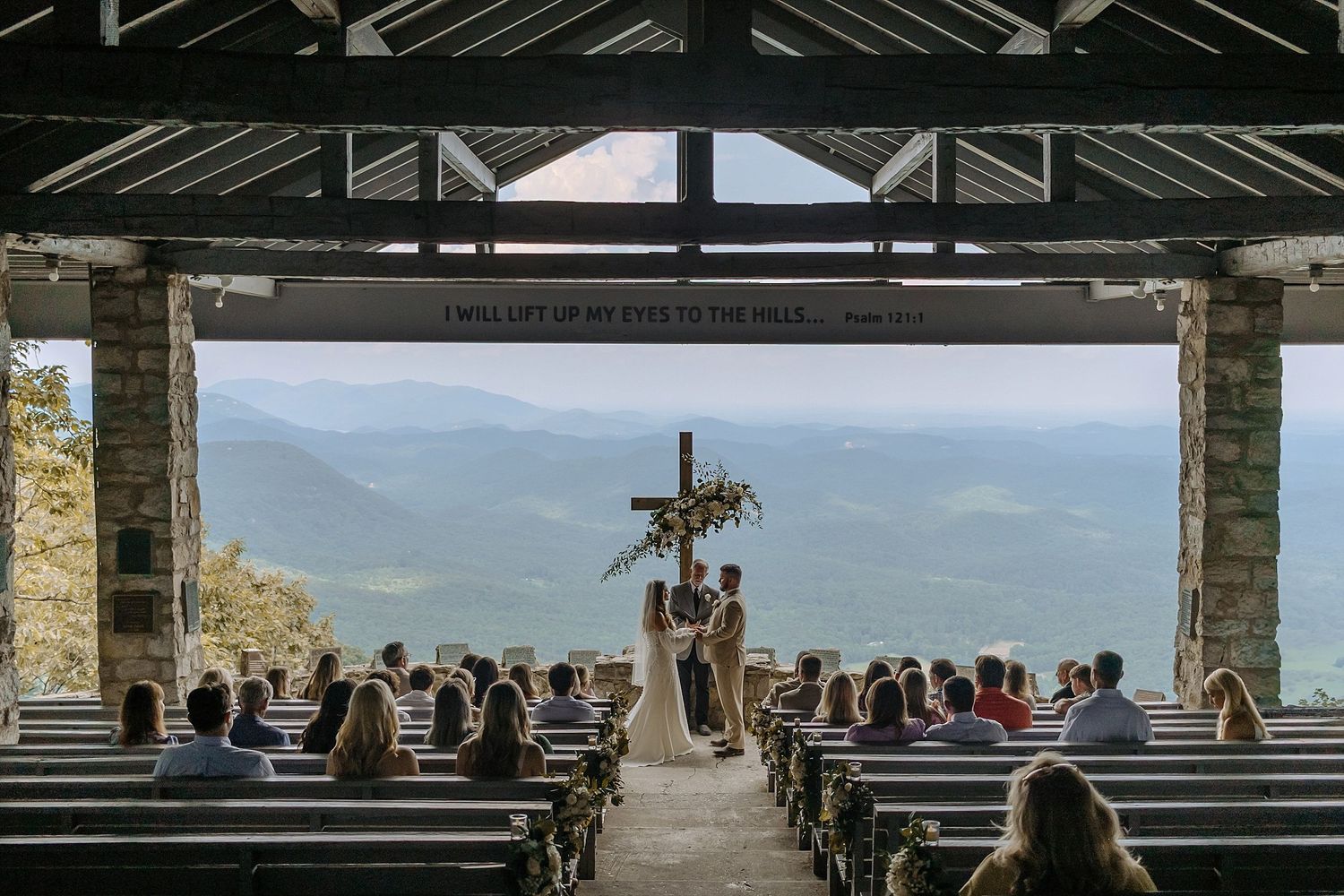A mountain chapel wedding ceremony with stunning valley views and wooden pews filled with guests.