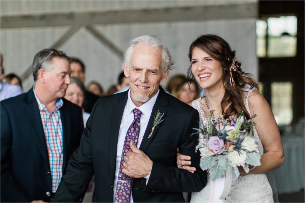Joyful wedding processional moment captured with laughter and smiles in rustic venue setting.