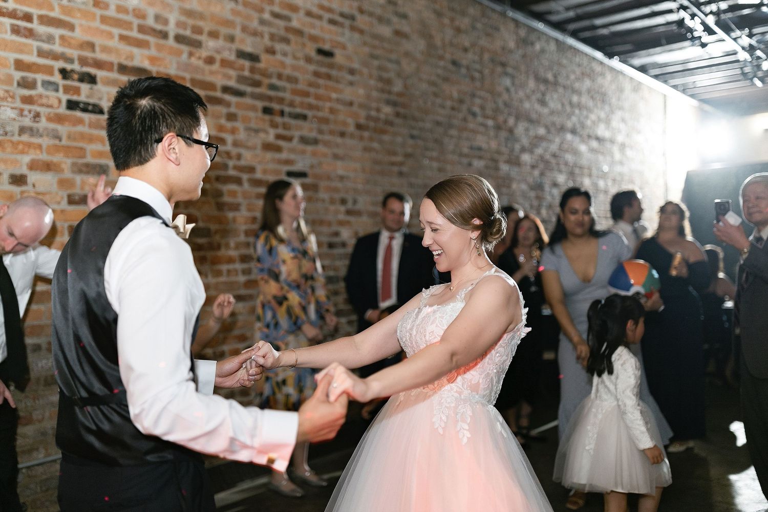 A couple shares a joyful moment while dancing together at a wedding reception in a rustic brick-walled venue.