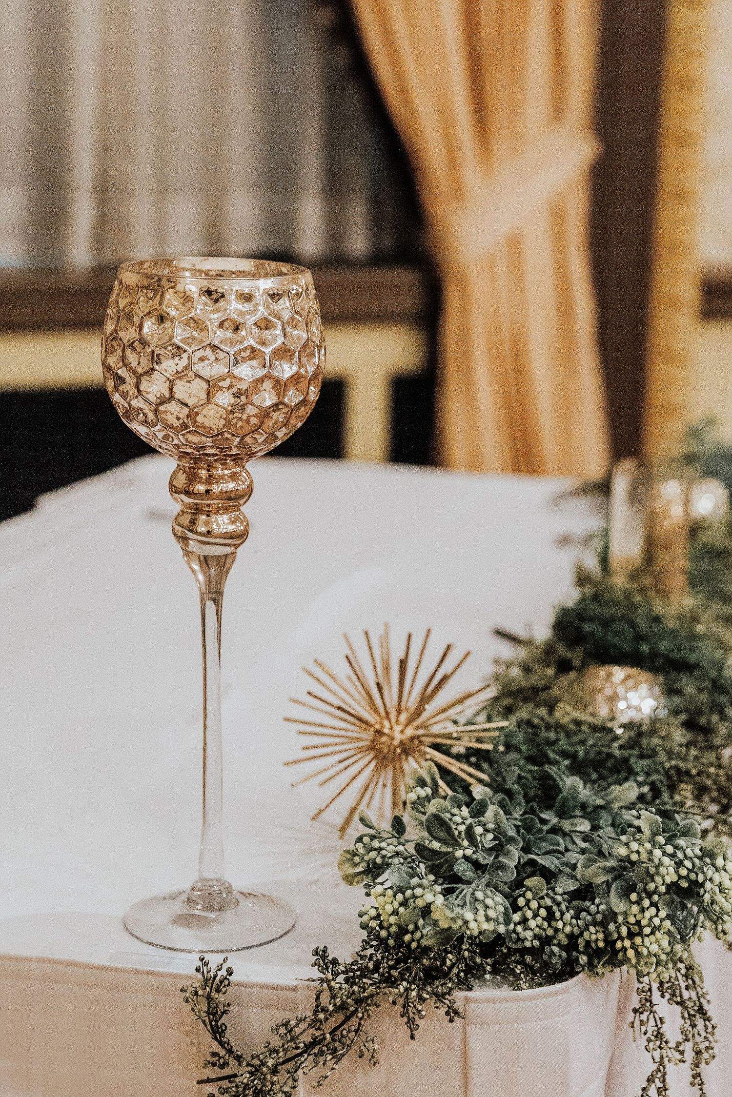 An ornate glass candleholder and gold decor accent a wedding reception table.