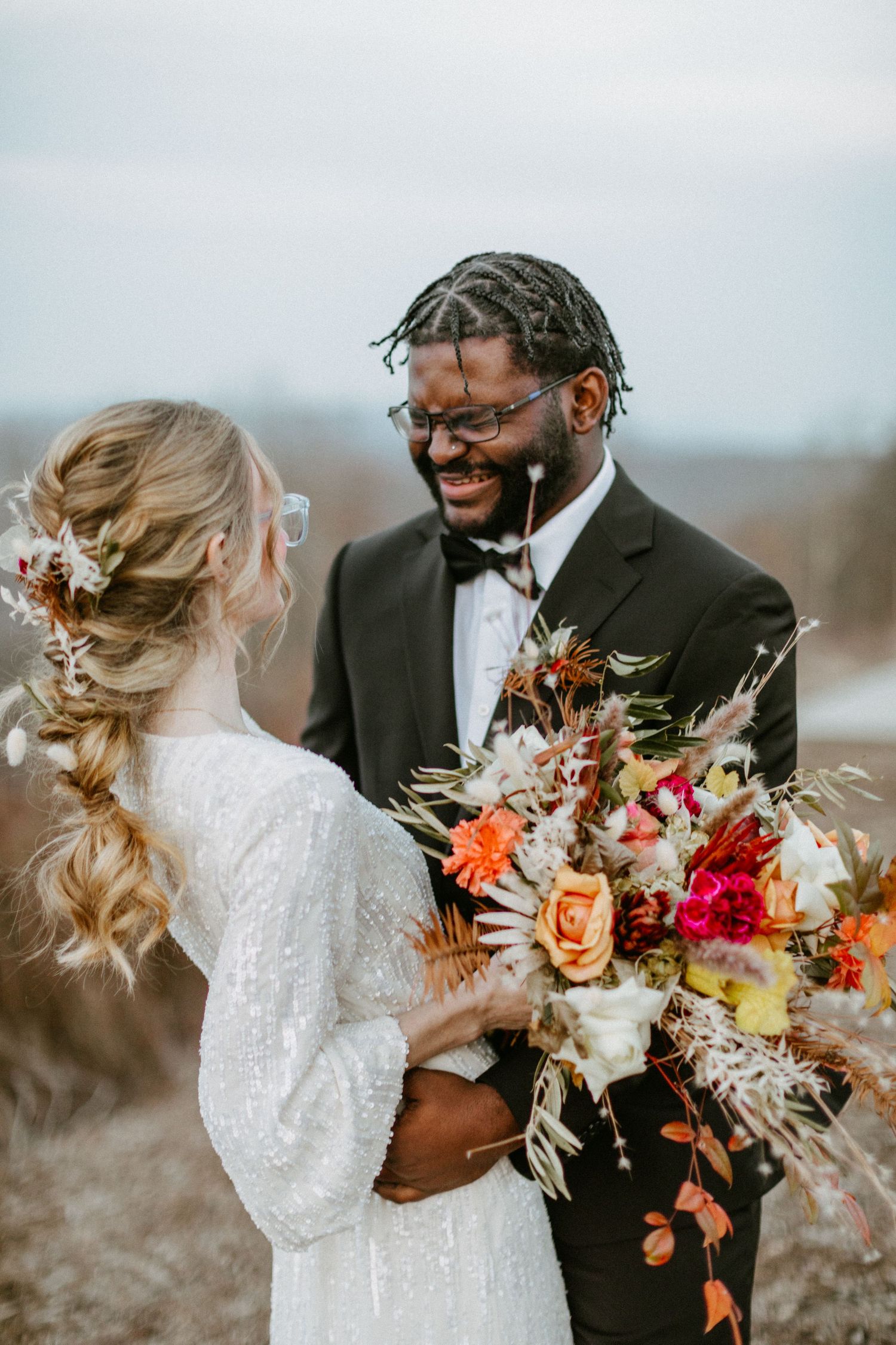 Joyful wedding couple sharing a moment while holding a vibrant autumn bouquet.
