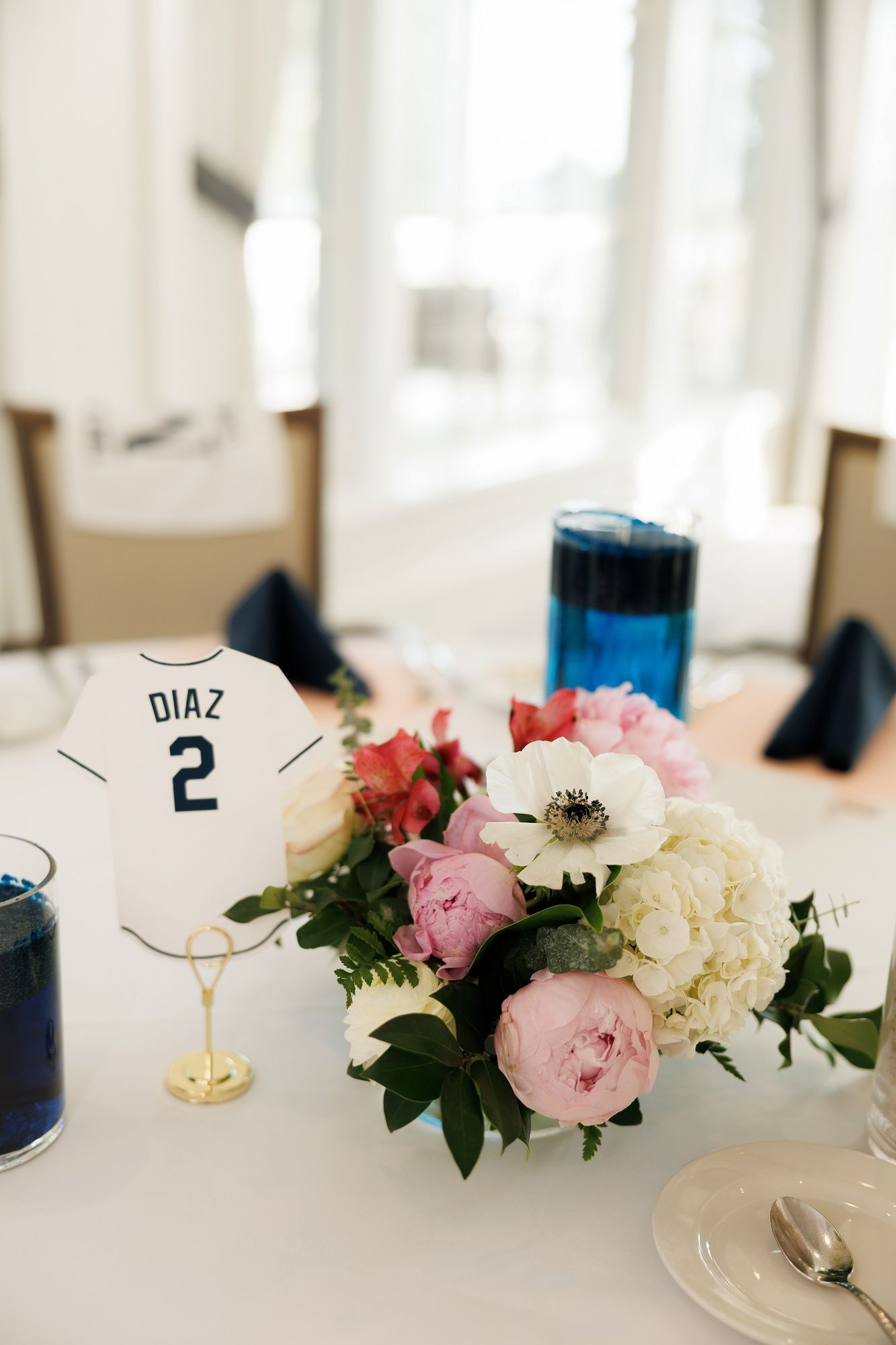 Elegant table settings with pink and white roses, navy accents, and name cards for a formal wedding reception.