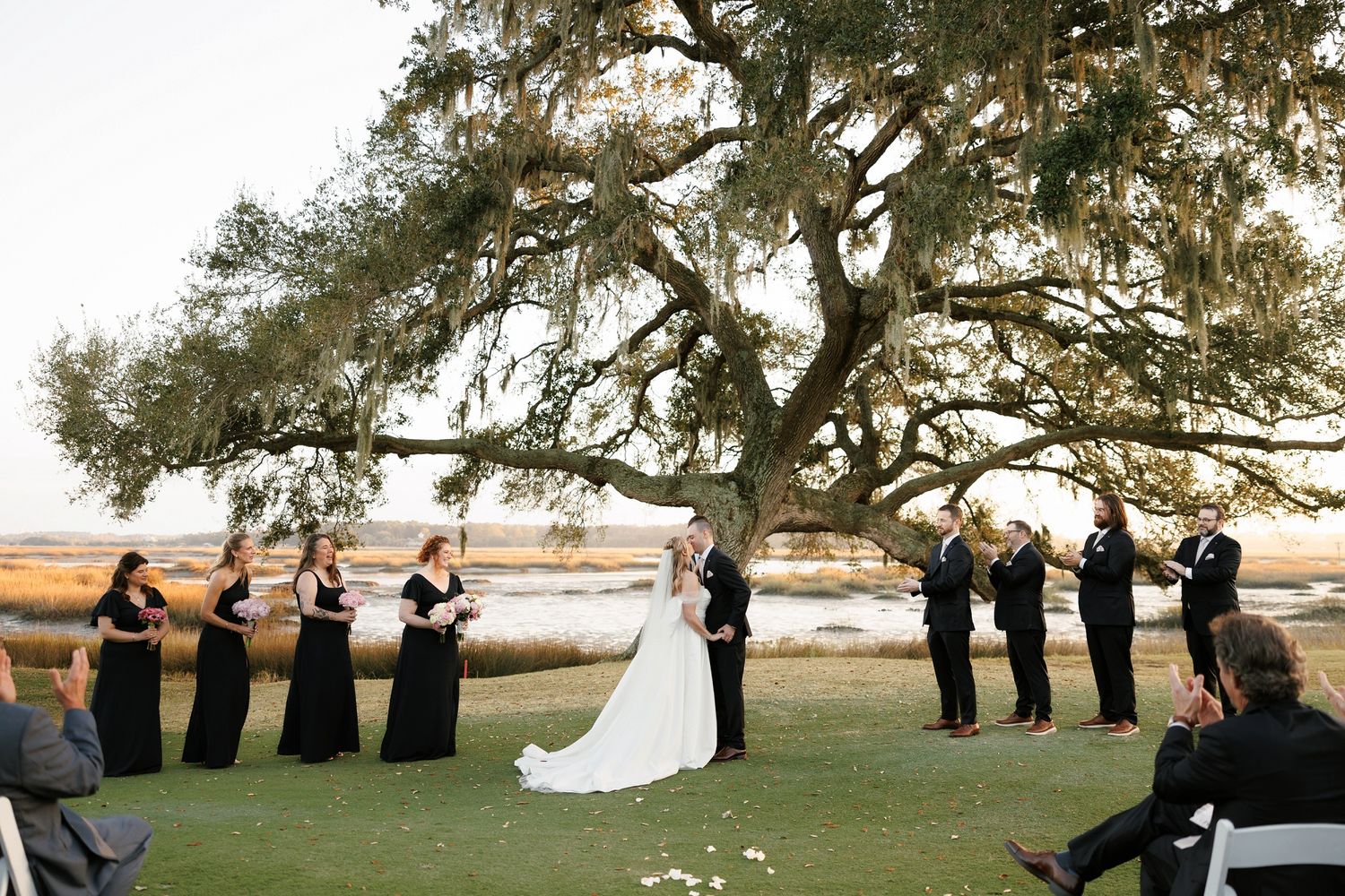 Wedding party lined up under majestic oak trees during an outdoor ceremony.