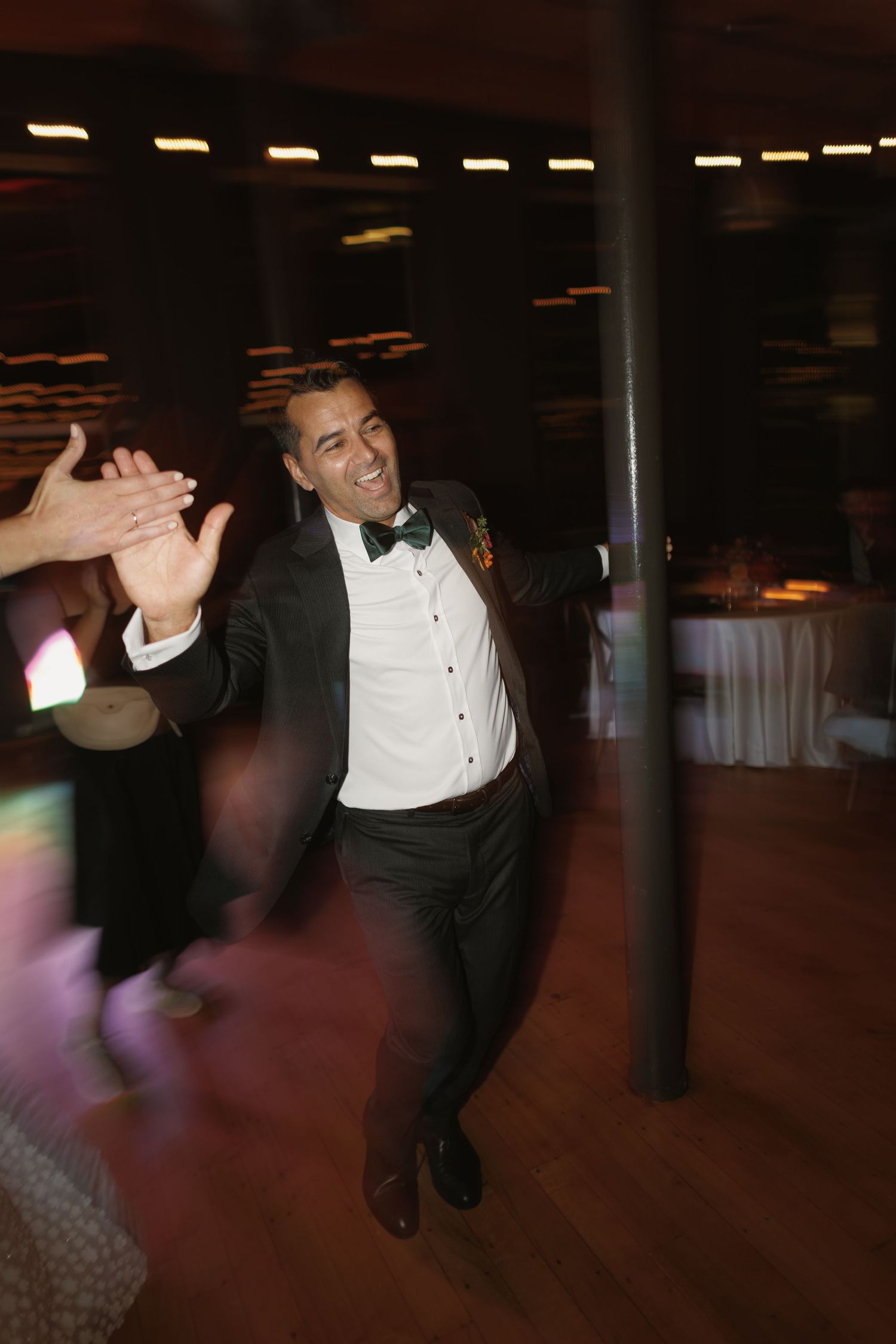 Groom in tuxedo high-fives guests while dancing energetically at lively wedding reception celebration.