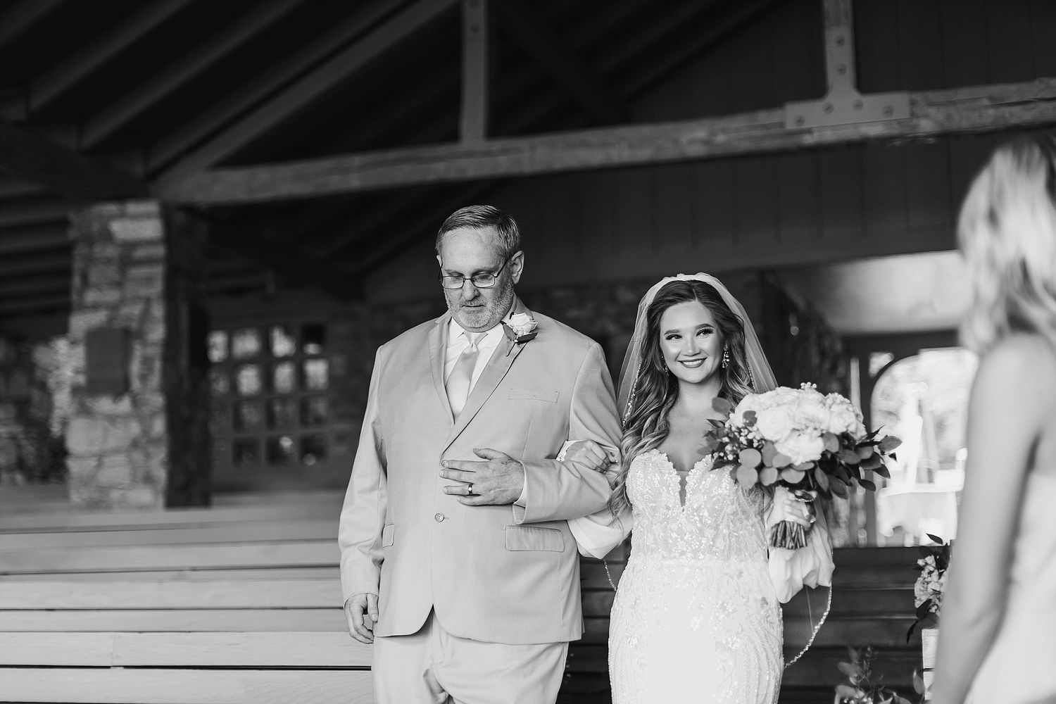 A black and white wedding processional moment captured at an elegant outdoor venue.