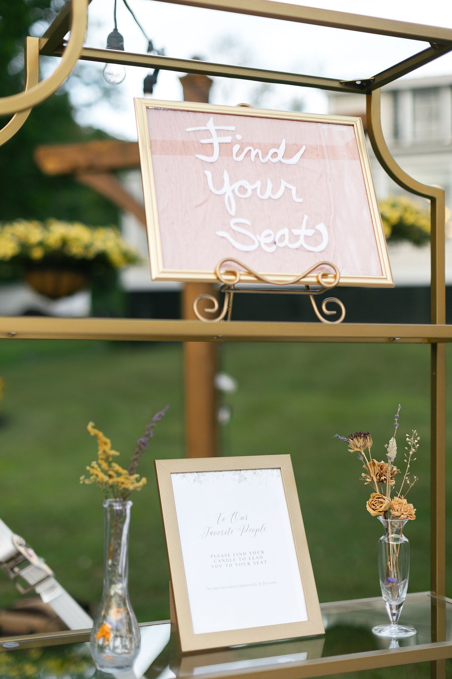 Pink and gold 'Find Your Seat' sign displayed on decorative stand with floral accents.