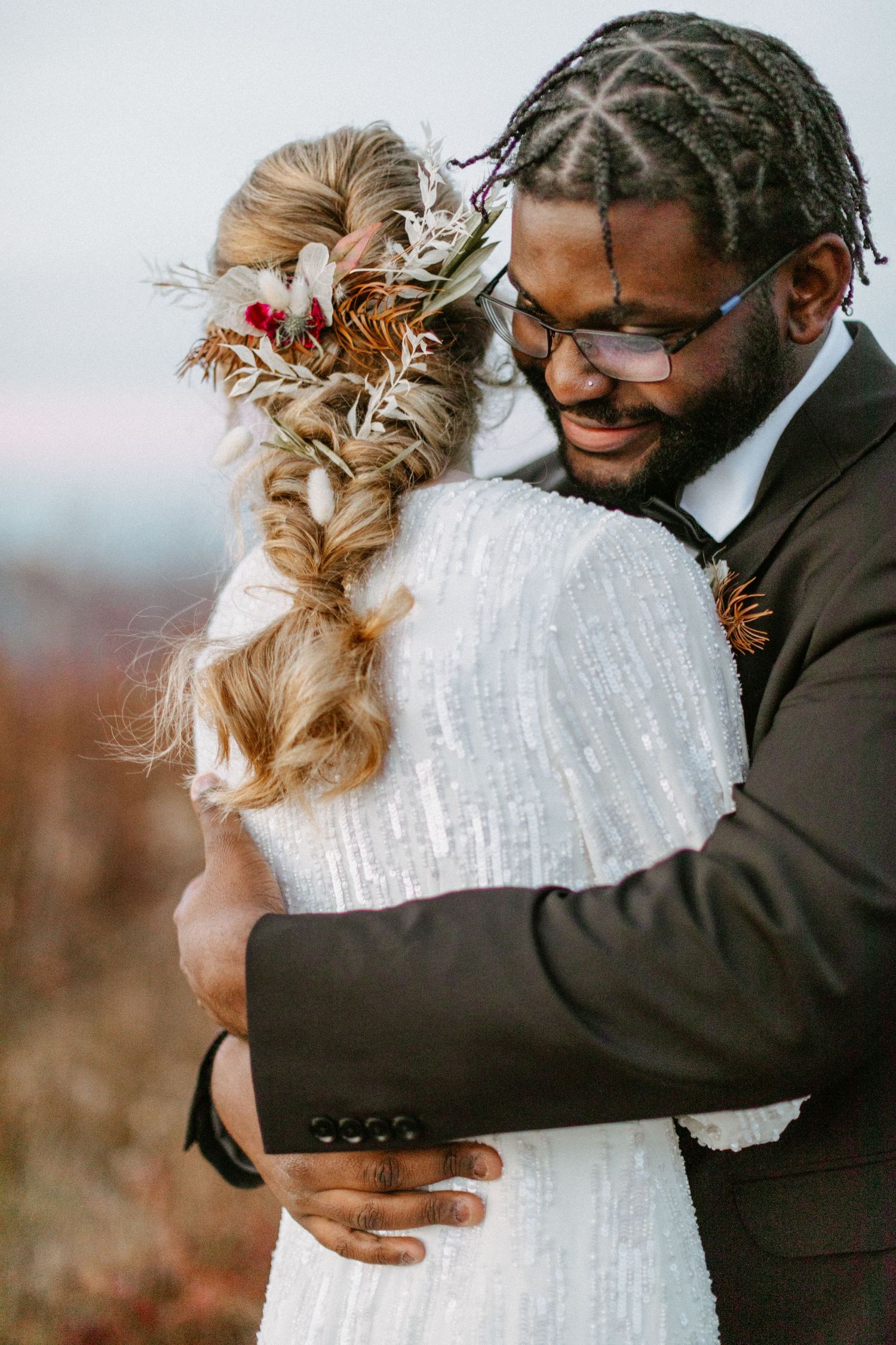 A tender embrace between a couple on their wedding day featuring a white lace dress and black suit.