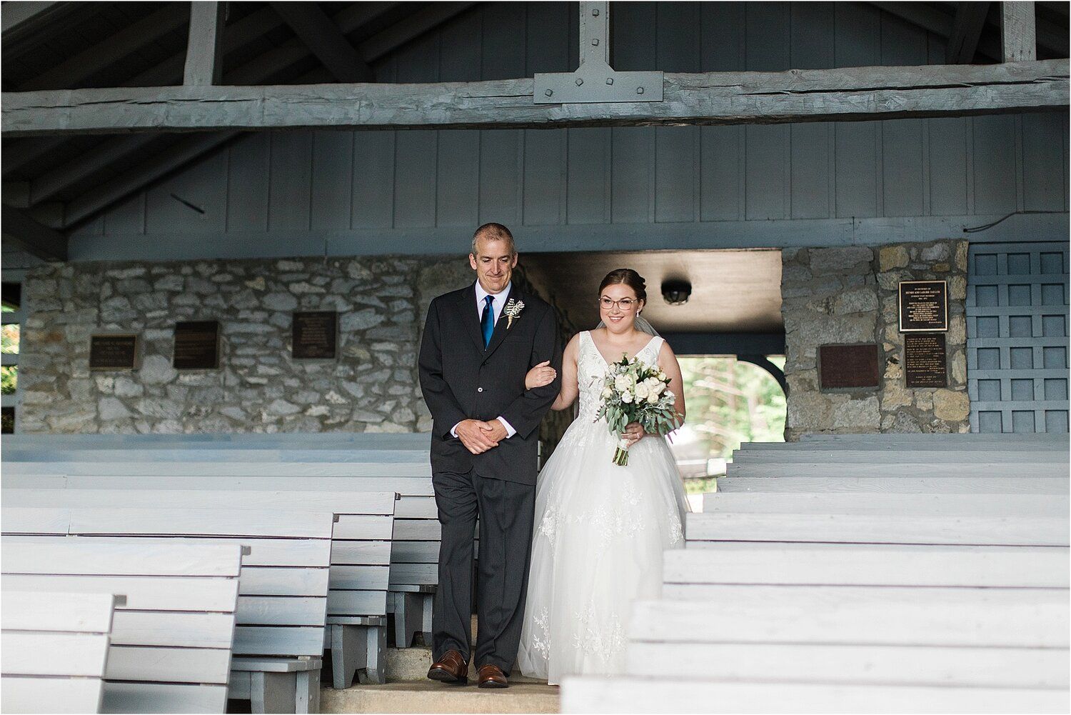 A wedding couple stands on stone steps of a rustic venue holding a white floral bouquet.