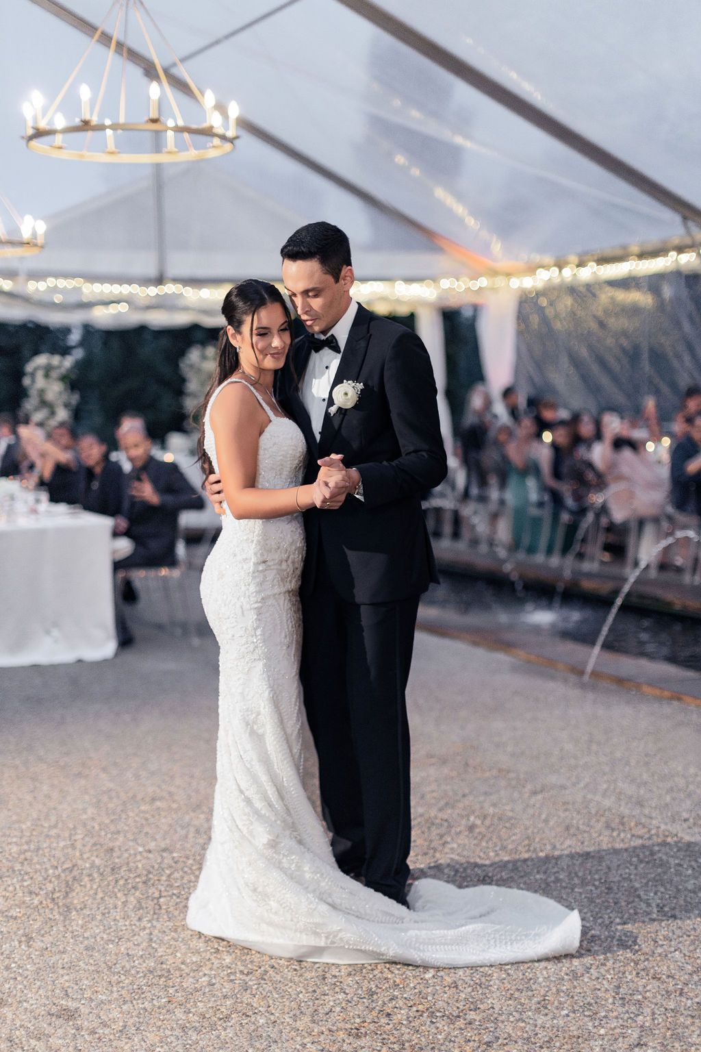 Romantic first dance moment under a crystal chandelier in a clear-top tent.