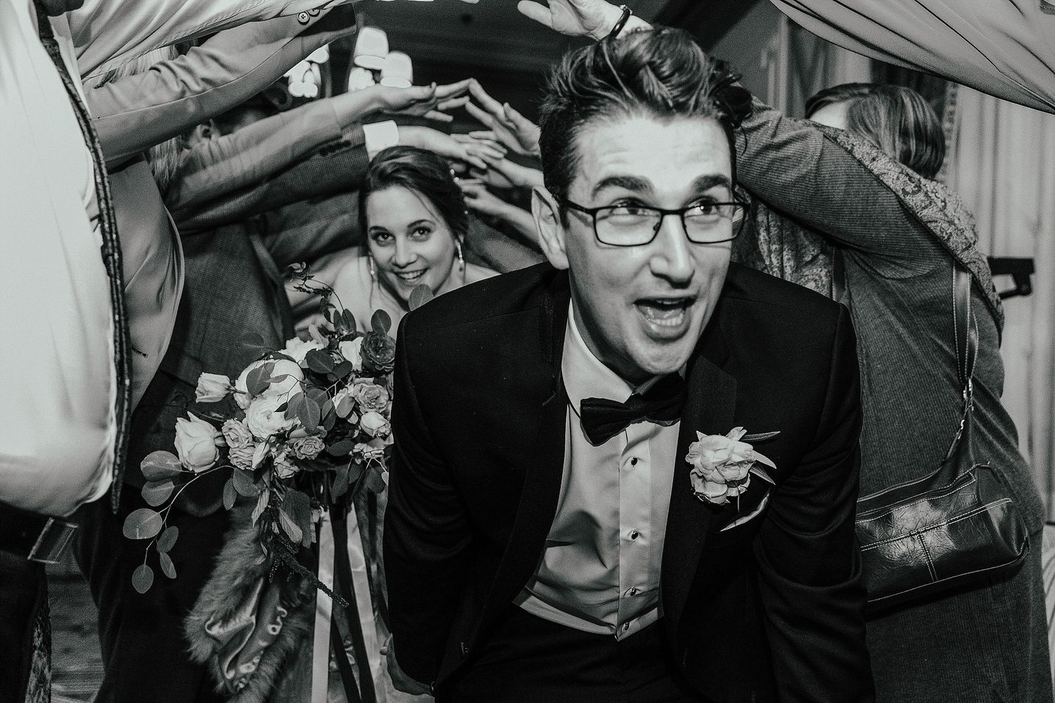 Black and white photo of wedding celebration with guests raising hands overhead.