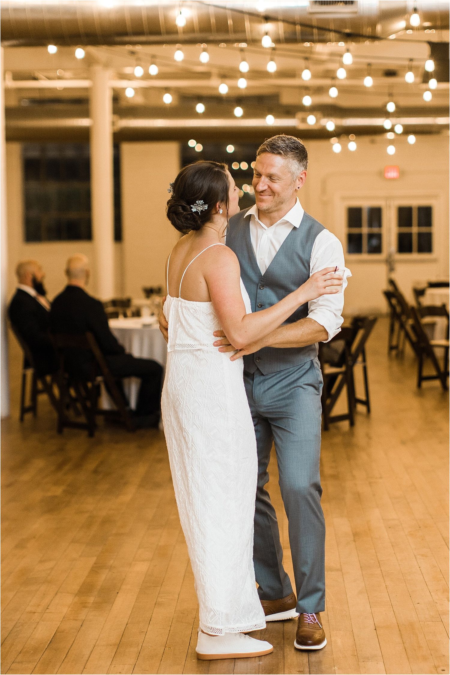 A couple shares a romantic dance under string lights in a reception venue.