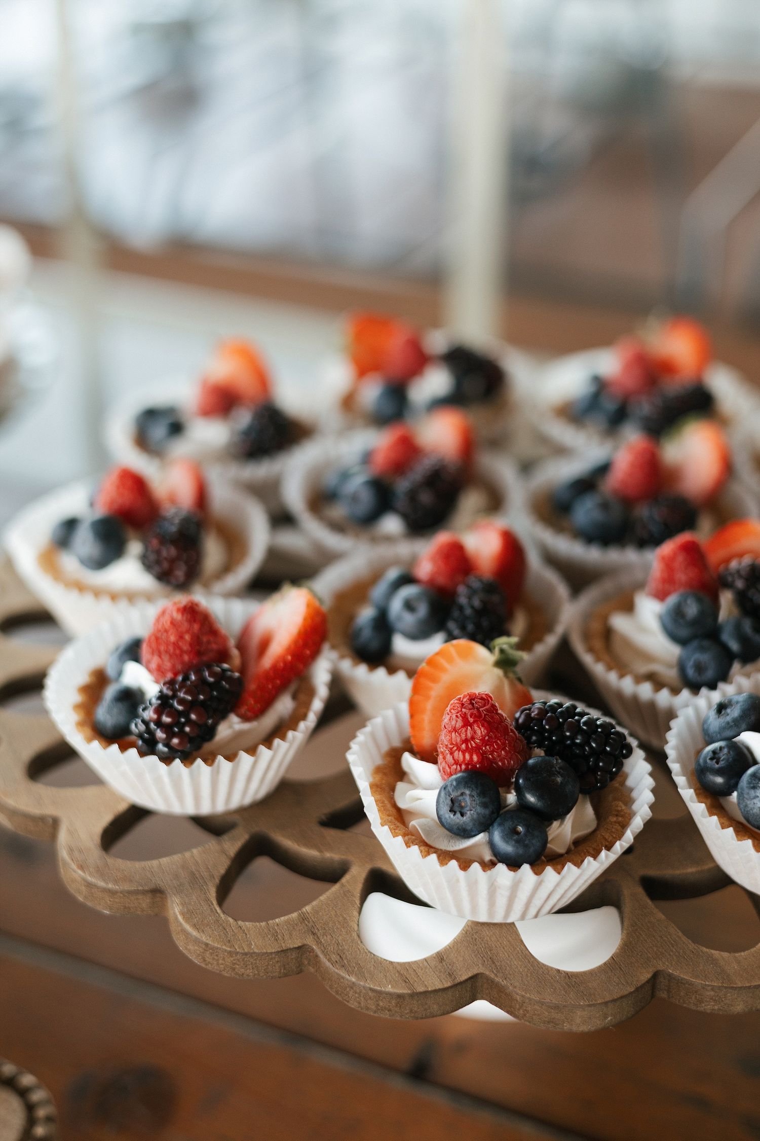 Mini dessert cups filled with fresh berries including strawberries, blackberries and blueberries displayed on a wooden stand.