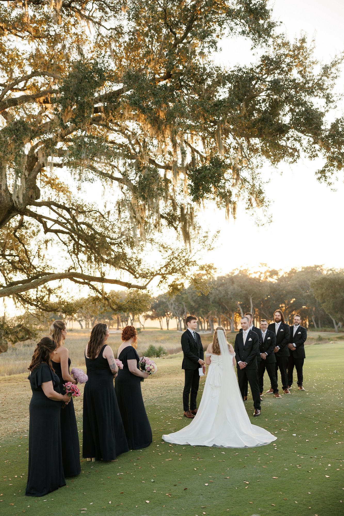 Wedding party lines up under Spanish moss draped trees during sunset ceremony.