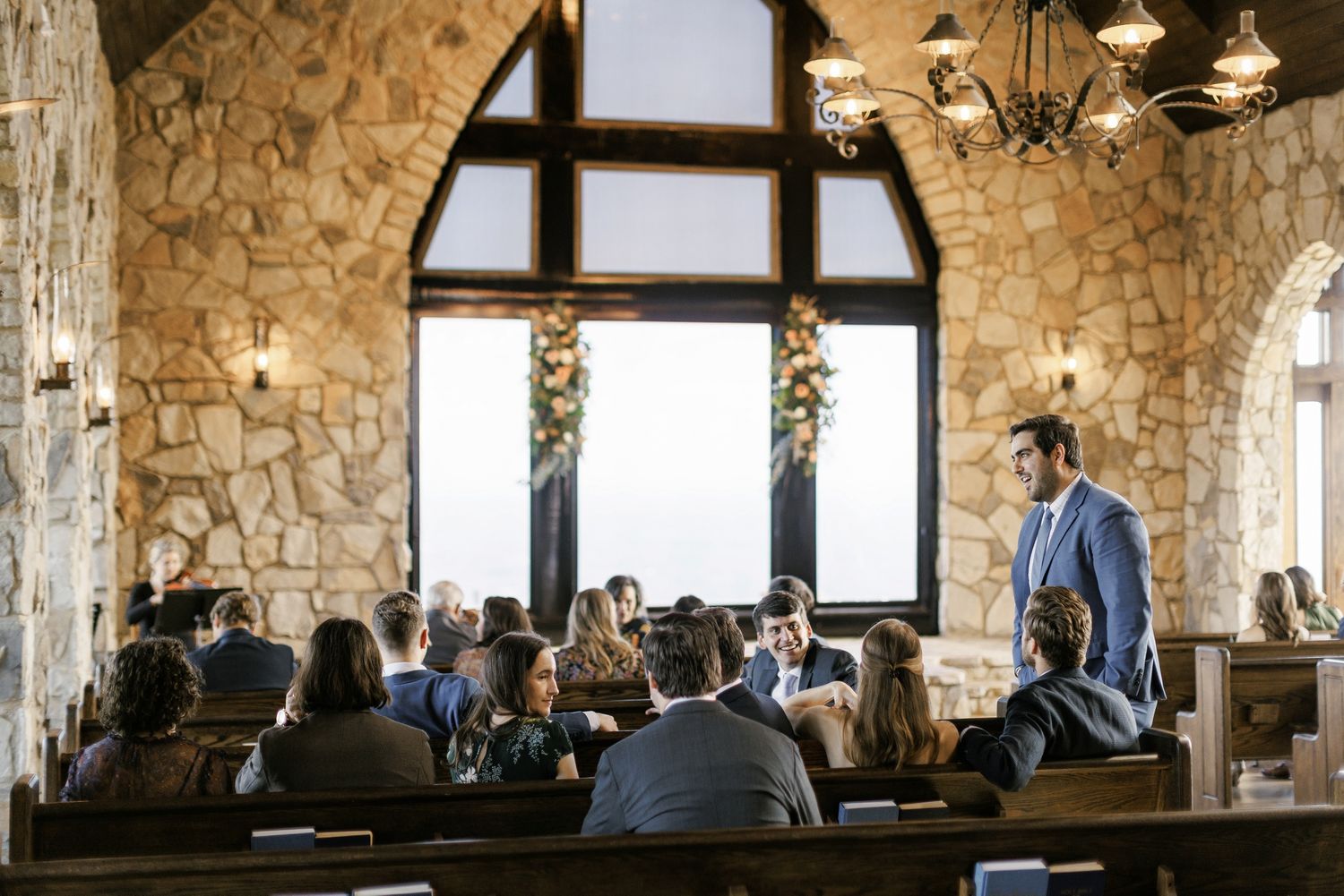 Interior of rustic stone banquet hall with exposed beams and large windows letting in natural light.