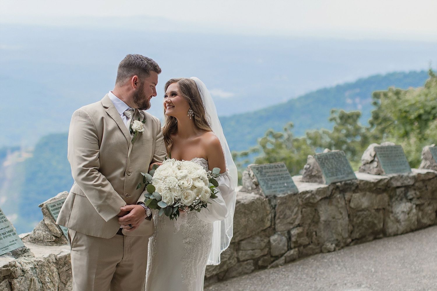 Couple sharing intimate moment at stone wall overlook with mountain views.