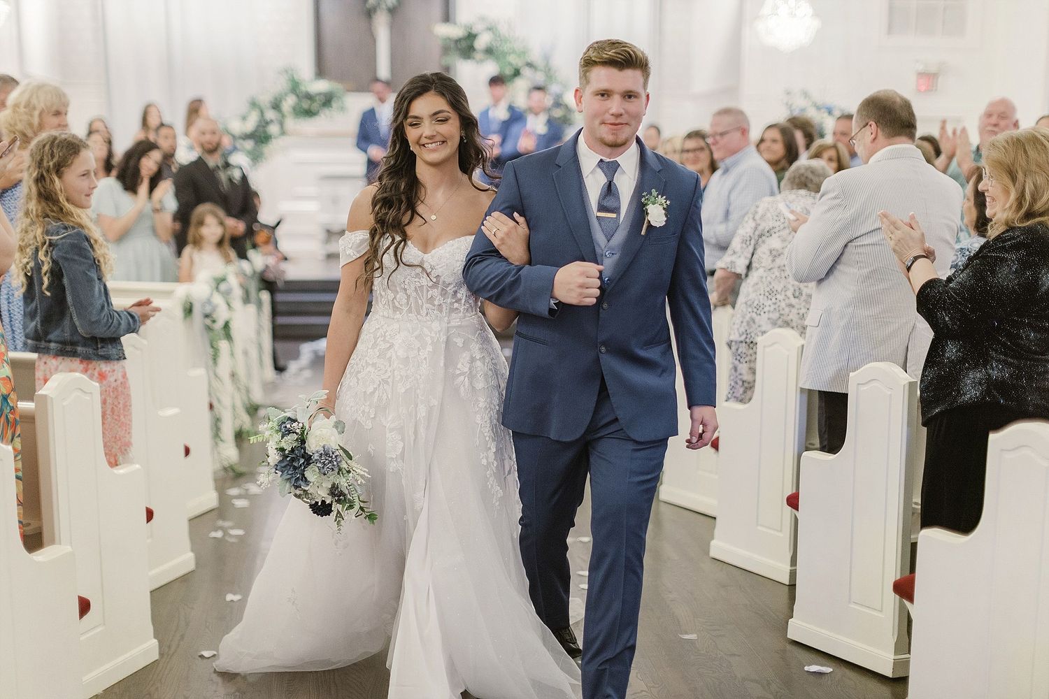 Newlyweds walk down church aisle while guests celebrate their joyous exit.